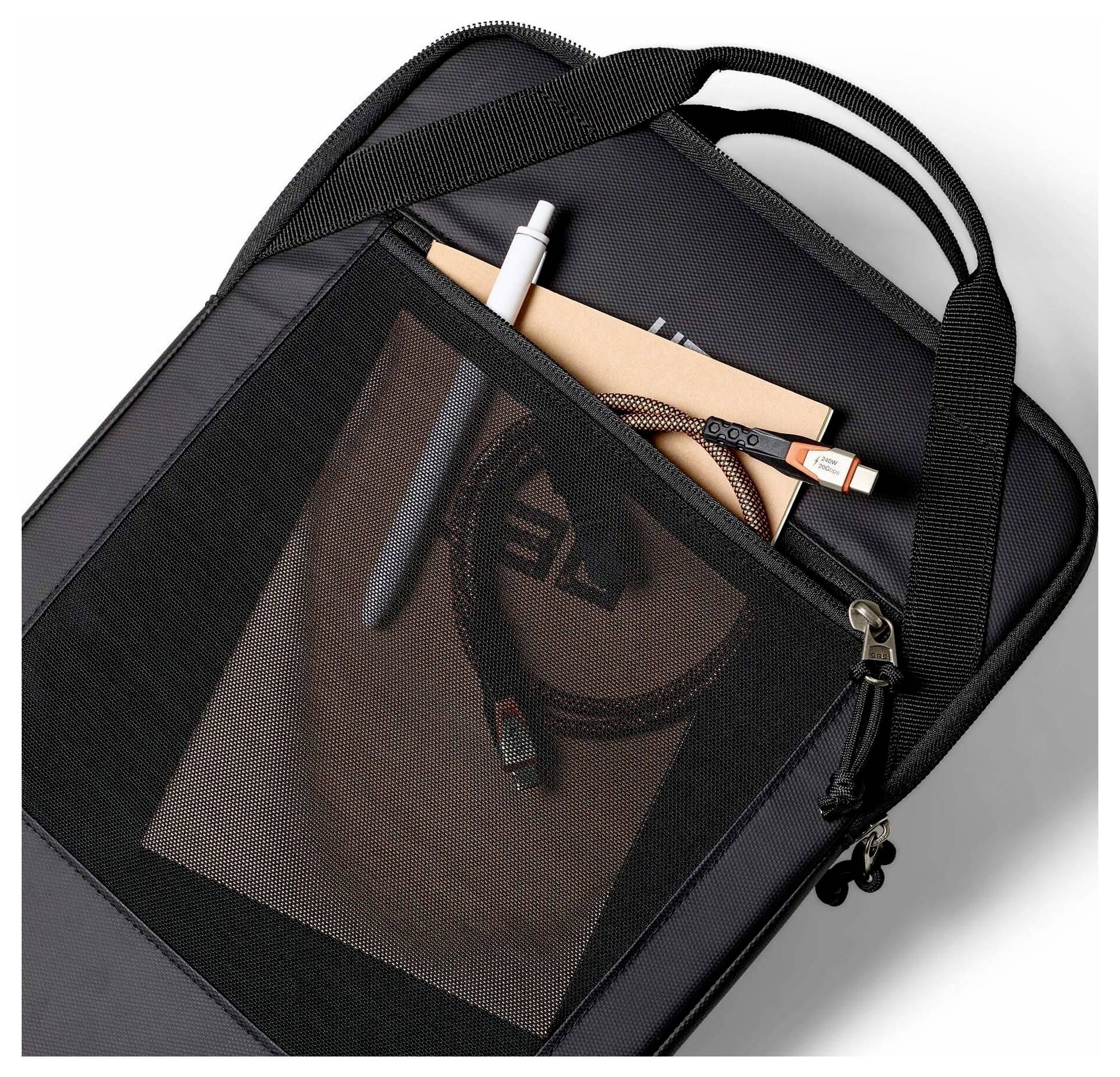 Schwarzer Rucksack mit vorderer Netzstofftasche, in der ein Ladekabel, ein Stift und ein Notizbuch sichtbar sind.