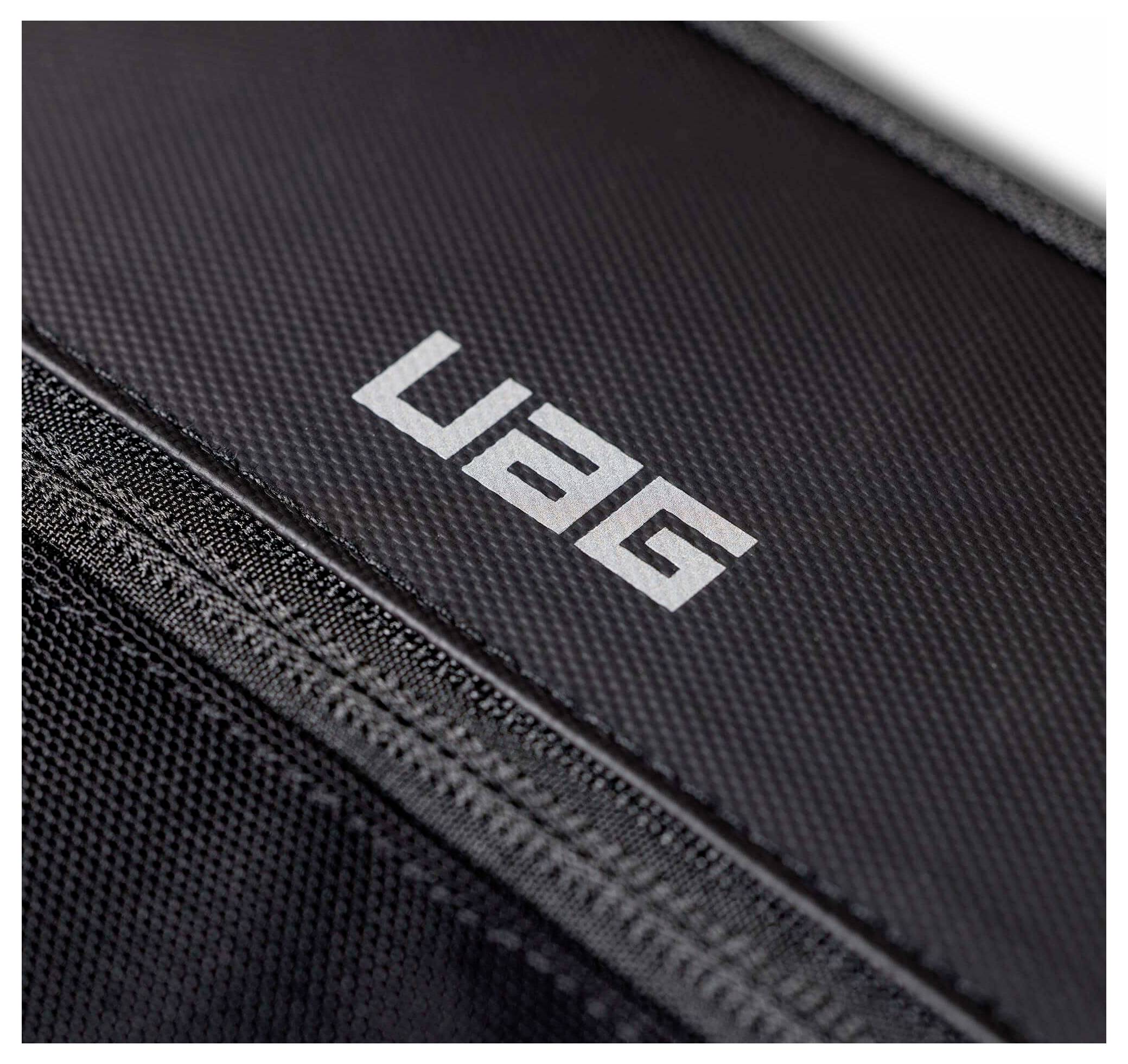 Nahaufnahme einer schwarzen strukturierten Tasche oder eines Koffers mit weißem „UAG"-Logo und einer sichtbaren Reißverschlussnaht.