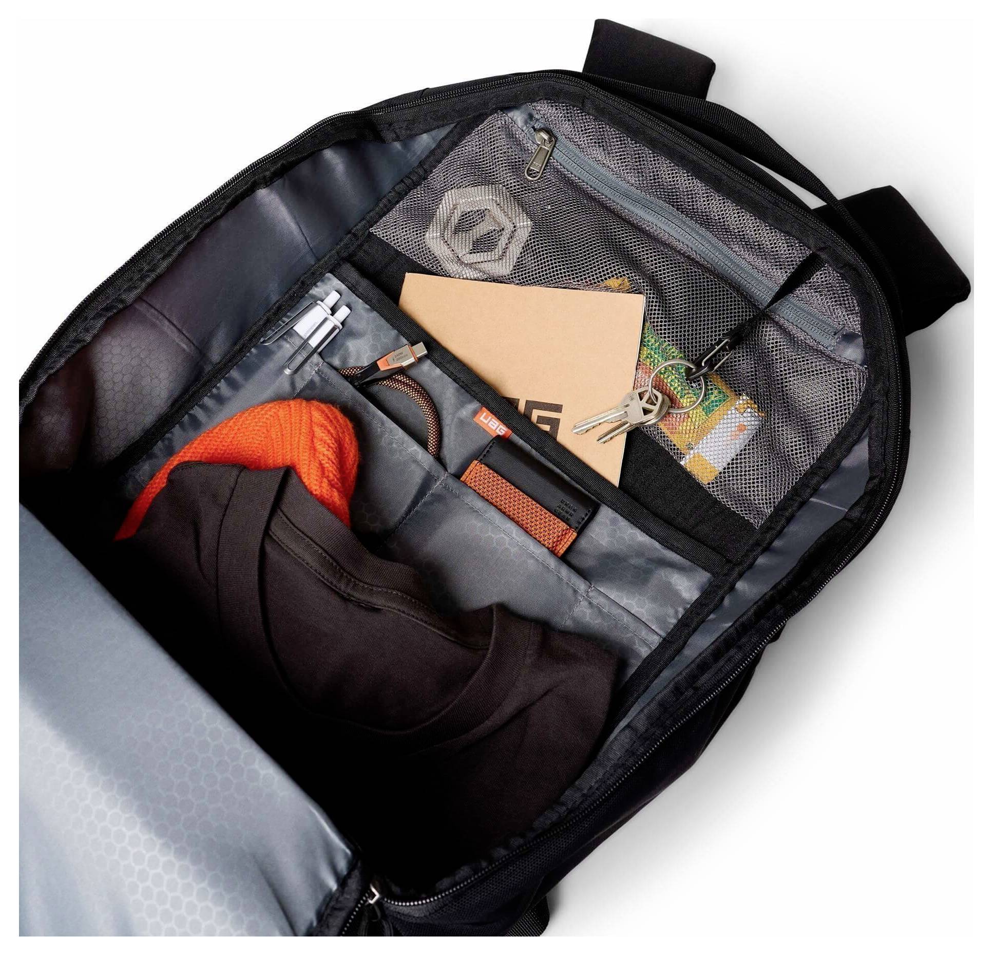 Offener Rucksack mit organisierten Inhalten, einschließlich einer Jacke, einem orangefarbenen Strickstück, einem Notizbuch, einem Stift, Schlüsseln und kleinen Accessoires in Netztaschen.