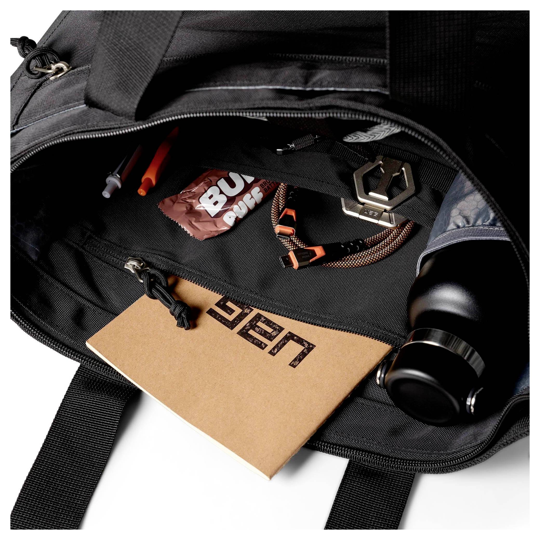 Schwarzer Rucksack teilweise offen mit sichtbarem Notizbuch, Wasserflasche, Snacks, Stiften und Schlüsseln im Inneren.