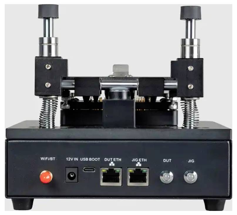Frontansicht eines schwarzen elektronischen Testgeräts/Prüfvorrichtung mit zwei vertikalen federbelasteten Klemmen, einem roten Netzschalter, USB- und Ethernet-Anschlüssen sowie gekennzeichneten DUT/JIG-Steckverbindern.