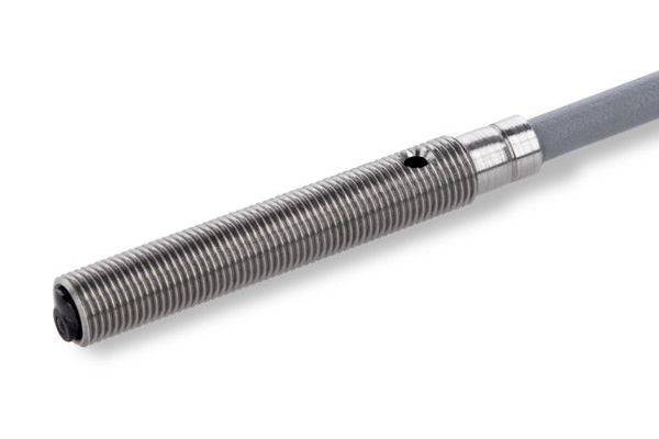 Nahaufnahme eines grauen zylindrischen Metallsensors oder einer Sonde mit Gewinde und einem angeschlossenen Kabel, dargestellt auf weißem Hintergrund.