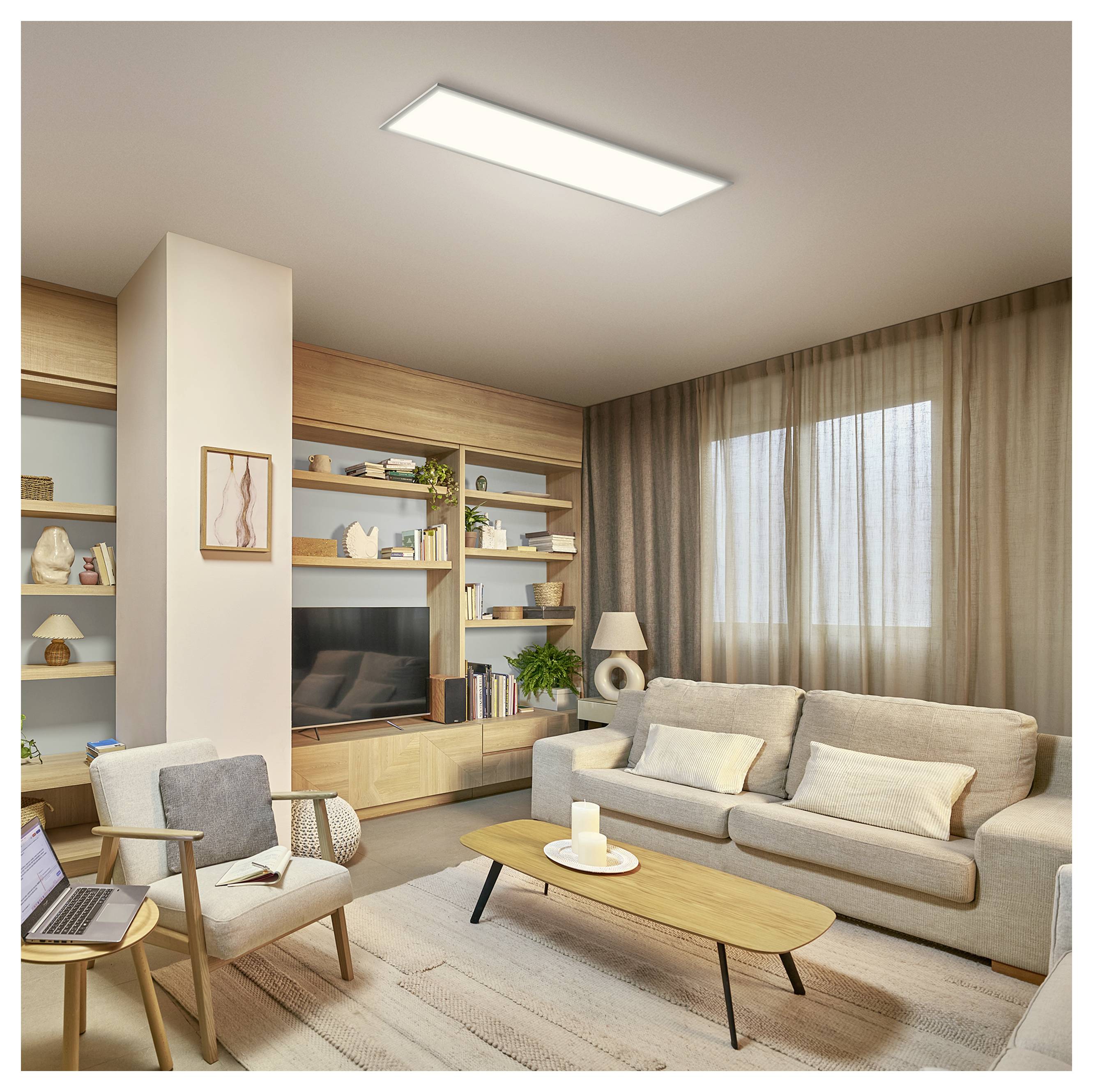 Modernes Wohnzimmer mit beigem Sofa, Sessel, Couchtisch, eingebauten Regalen, Fernseher und einem großen Fenster mit transparenten Vorhängen.