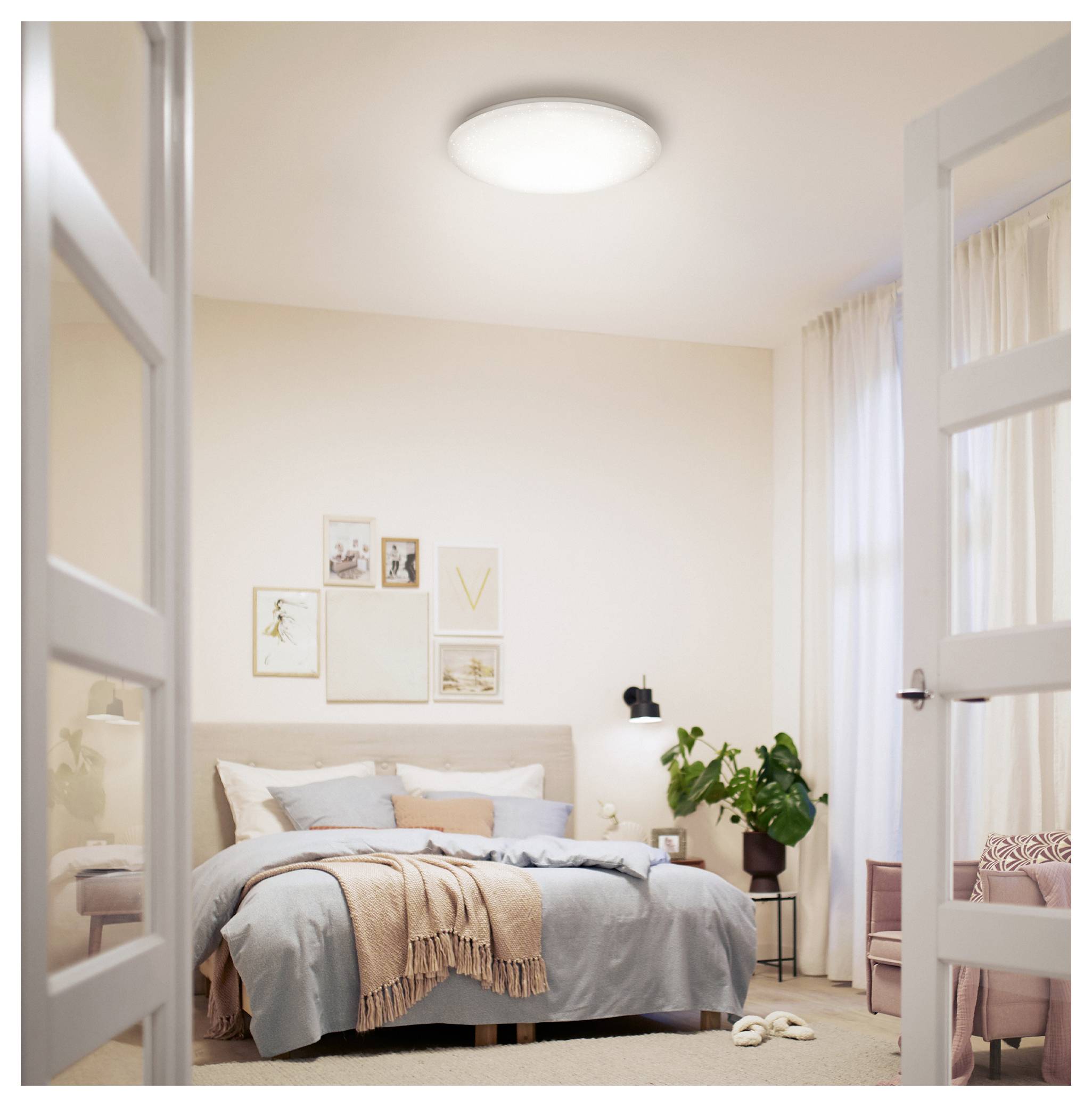 Gemütliches Schlafzimmer mit ordentlich gemachtem Bett, gerahmten Wandbildern, Topfpflanze und offenen französischen Türen, die ins Zimmer führen.
