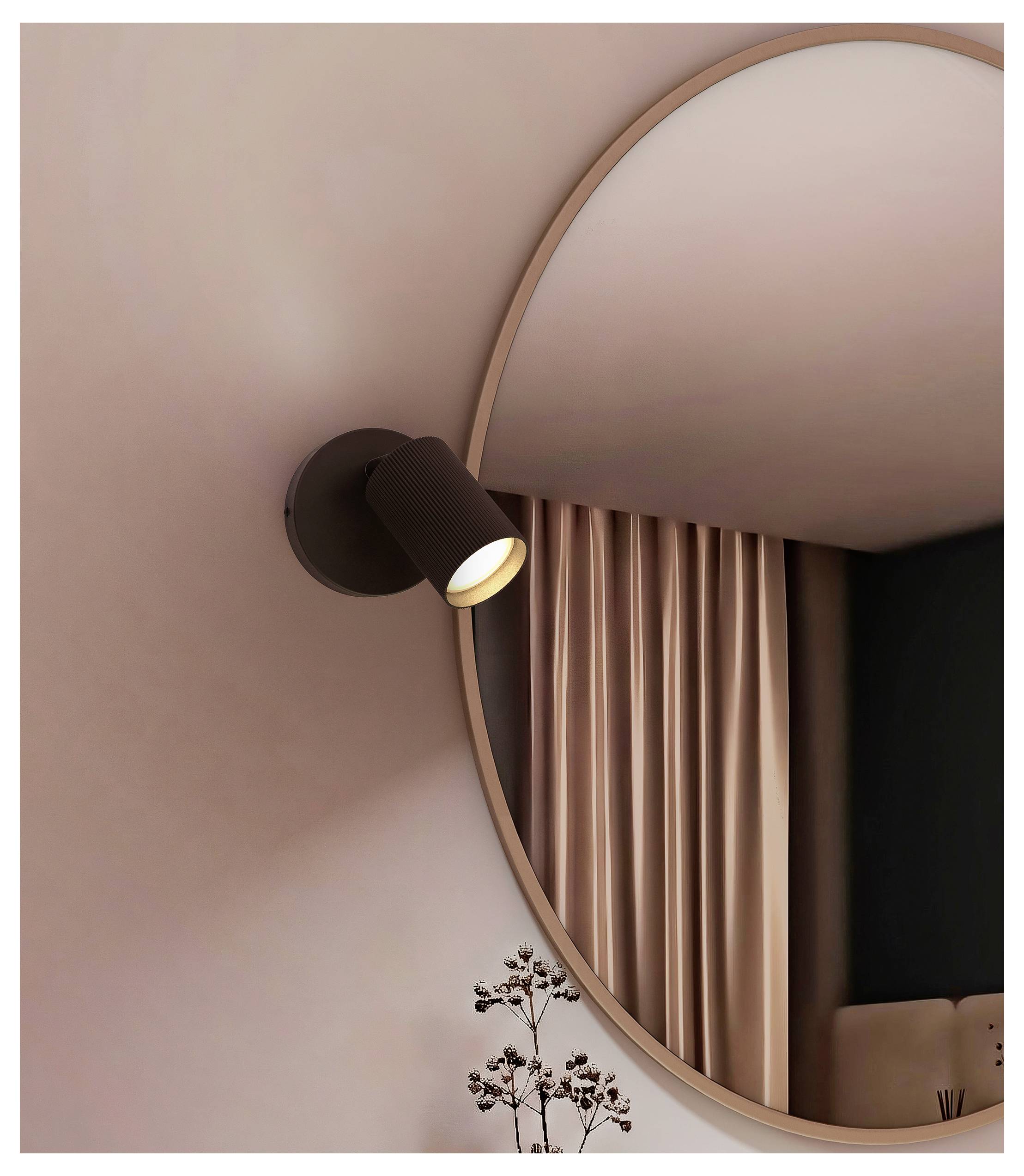 Moderne Wandleuchte mit einem schwarzen Strahler neben einem großen runden Spiegel, der rosa Gardinen in einem minimalistischen Raum reflektiert.