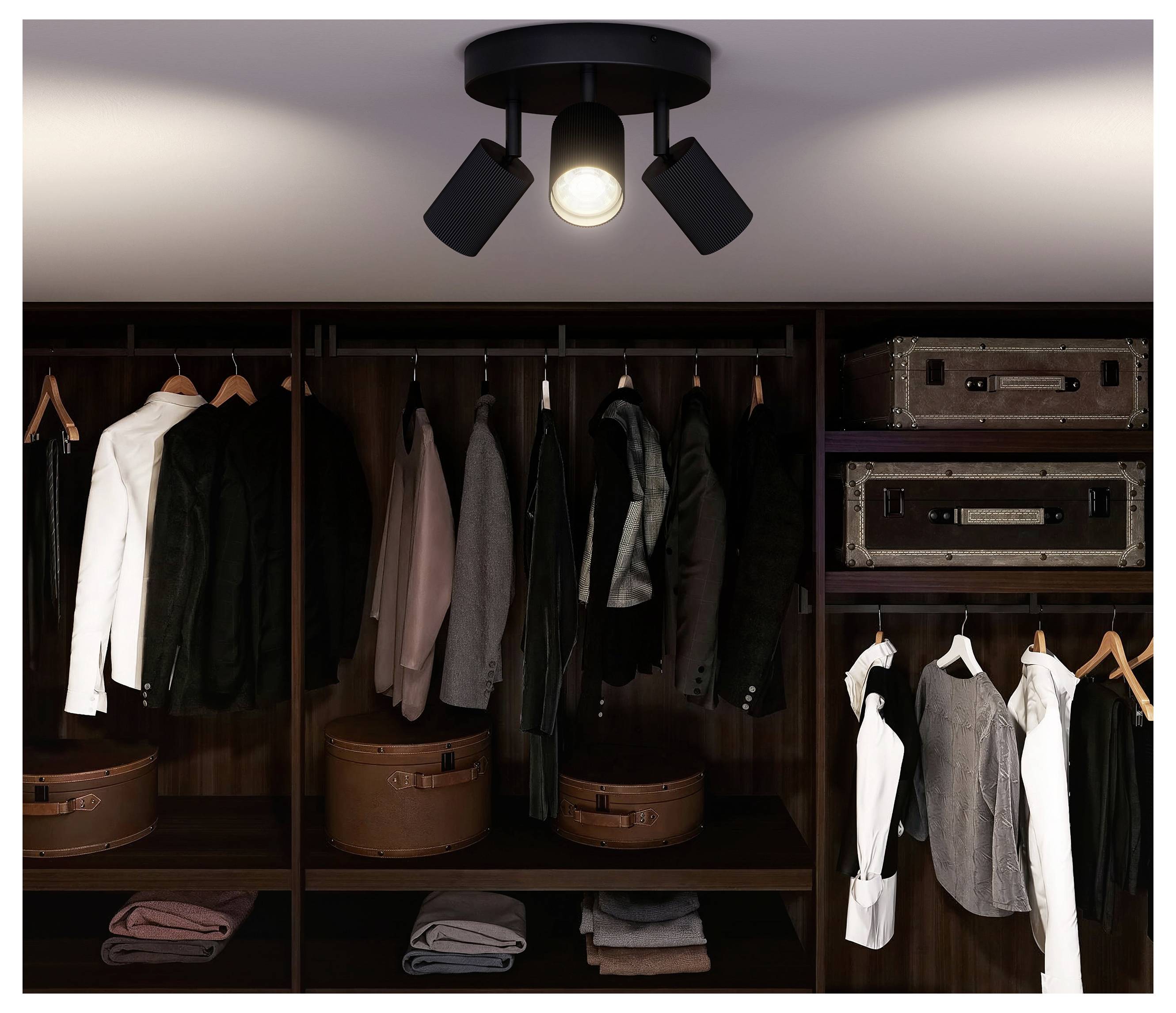 Begehbarer Kleiderschrank mit dunklem Holzregal, hängenden Jacken und Hemden, gefalteter Kleidung, Koffern und einer Deckenleuchte.