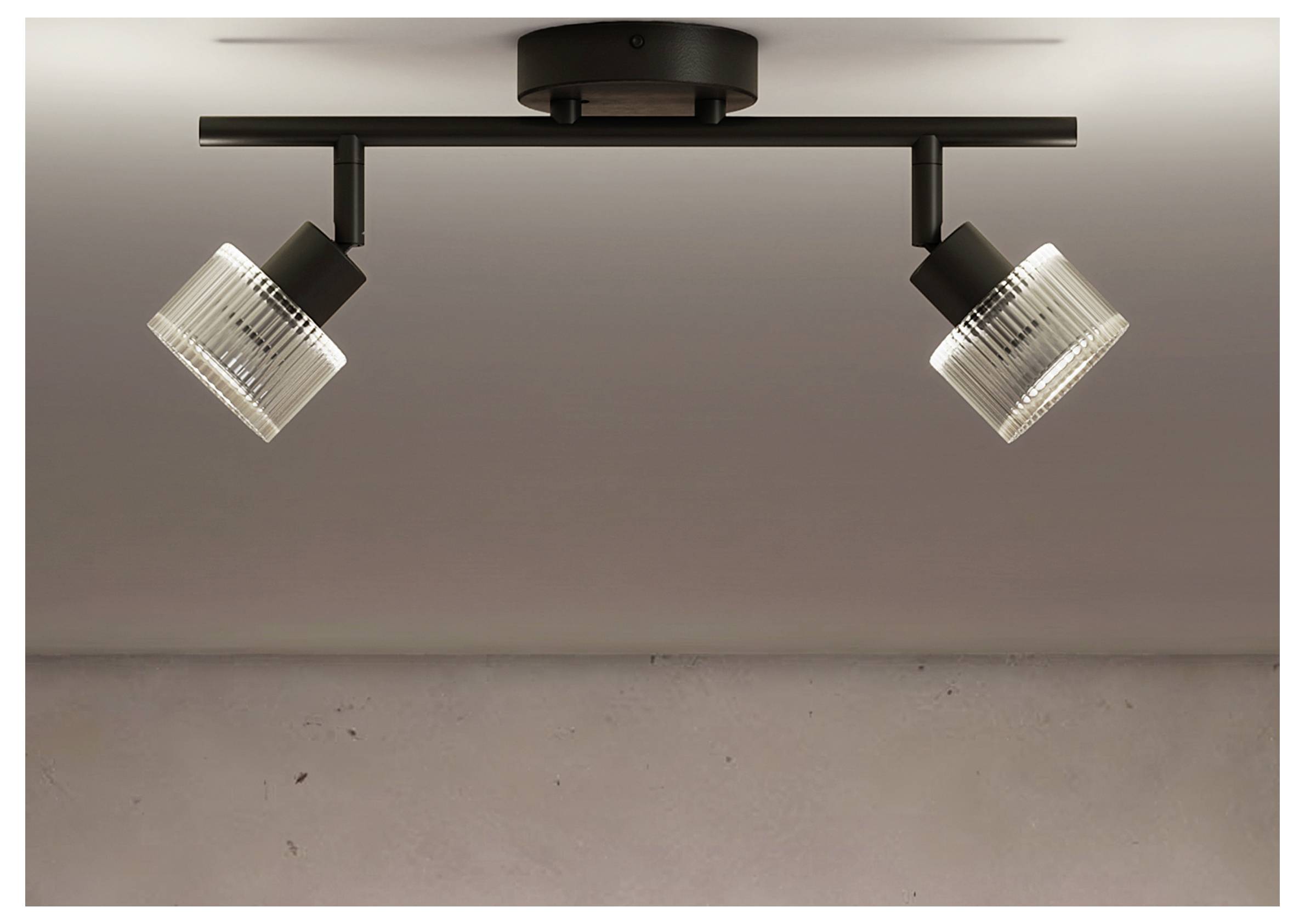 Schwarze Deckenleuchte mit zwei verstellbaren gerippten Glas-Spotlights, die auf einer horizontalen Schiene gegen eine glatte Wand montiert sind.