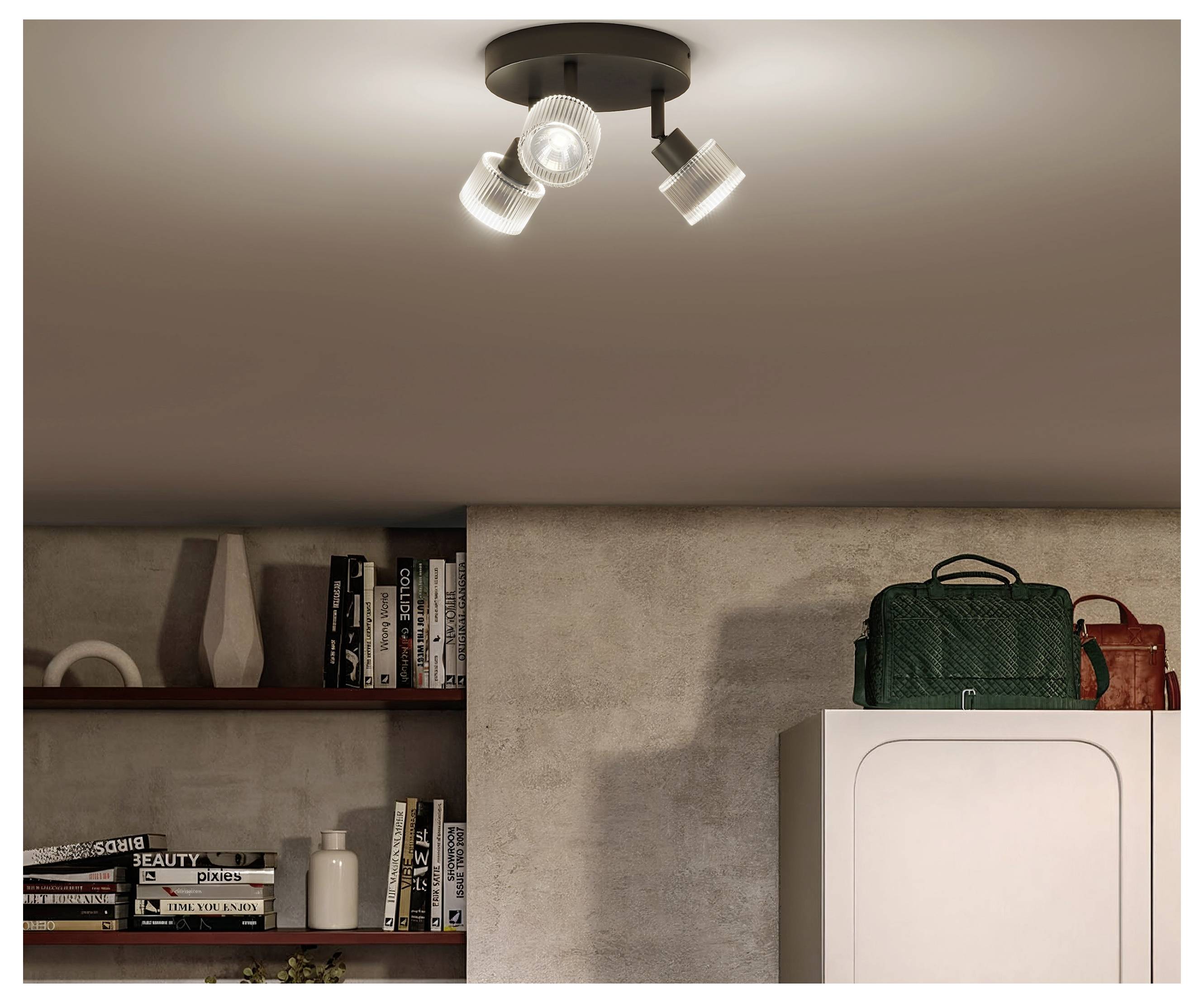 Innenzimmer mit Deckenspot, eingebauten Regalen mit Büchern und Dekoration sowie ein Schrank, der mit grünen und roten Taschen bedeckt ist