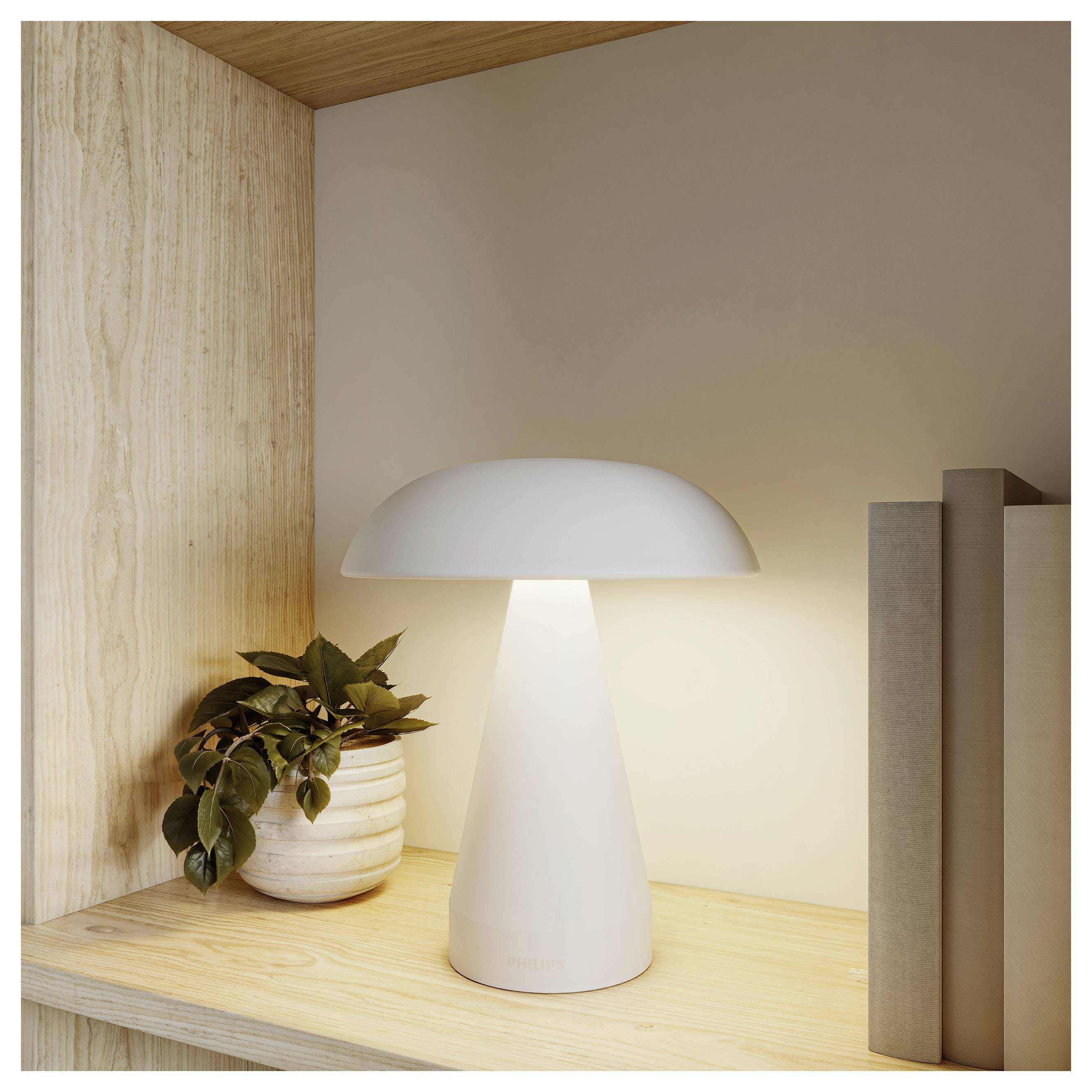 Moderne pilzförmige weiße Tischlampe, die auf einem Holzregal neben einer Topfpflanze und Büchern in einer minimalistischen Nische leuchtet.