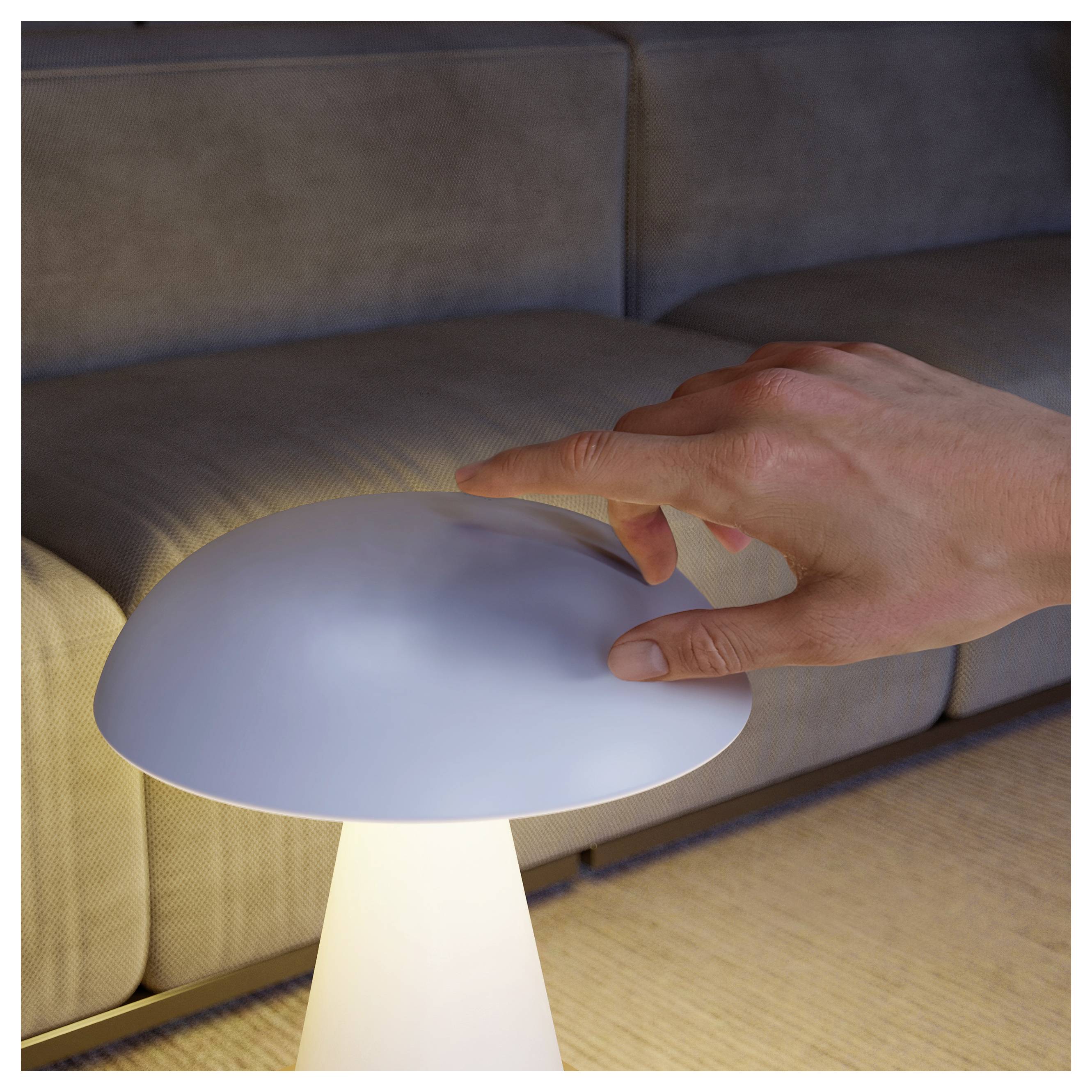 Eine Hand greift danach, die leuchtende Kuppel einer kleinen Tischlampe neben einem Sofa in einem düsteren Wohnzimmer zu berühren.