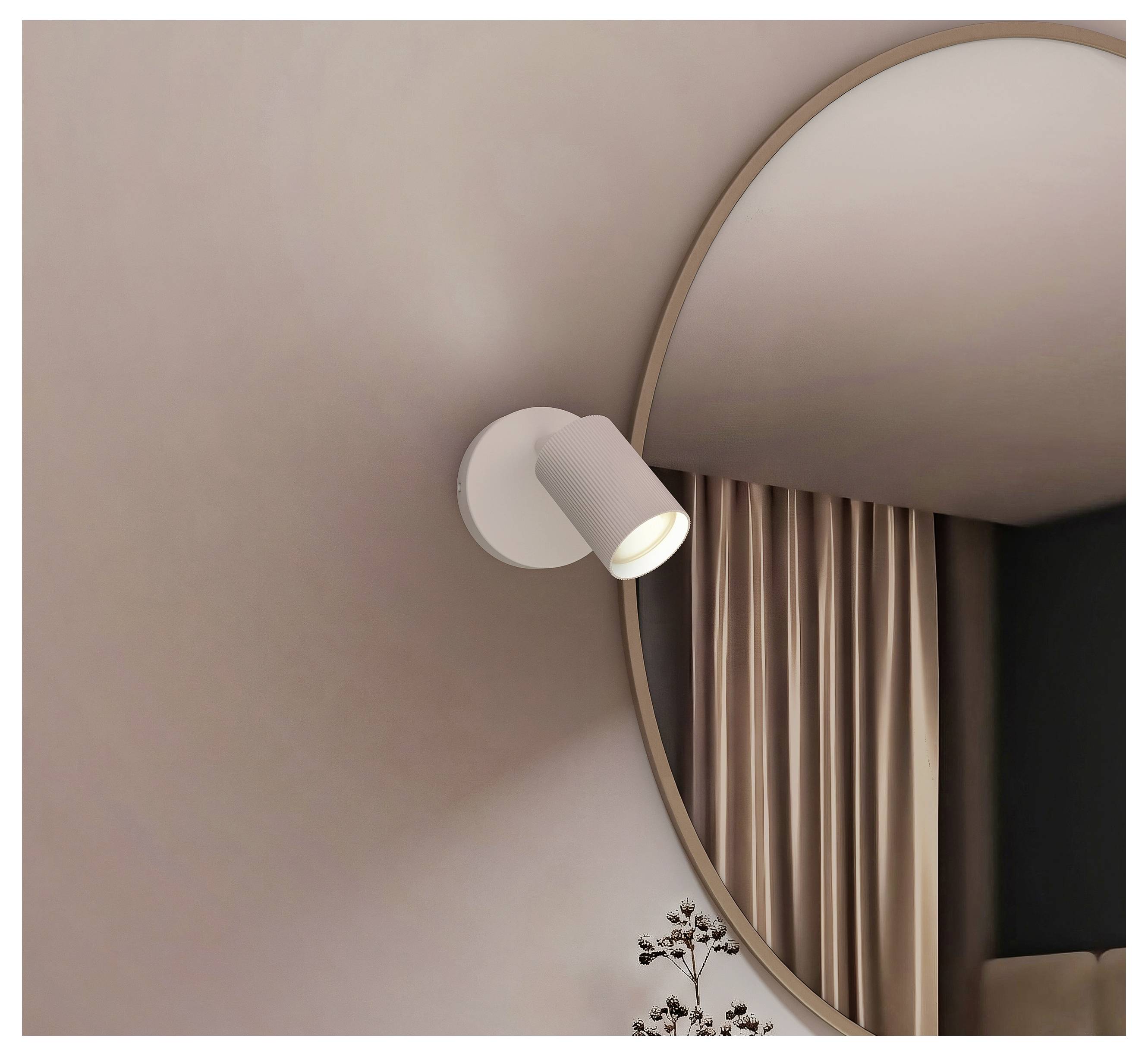 An der Wand montierter Strahler neben einem großen runden Spiegel, reflektiert mit beigefarbenen Vorhängen in einem minimalistischen Interieur.