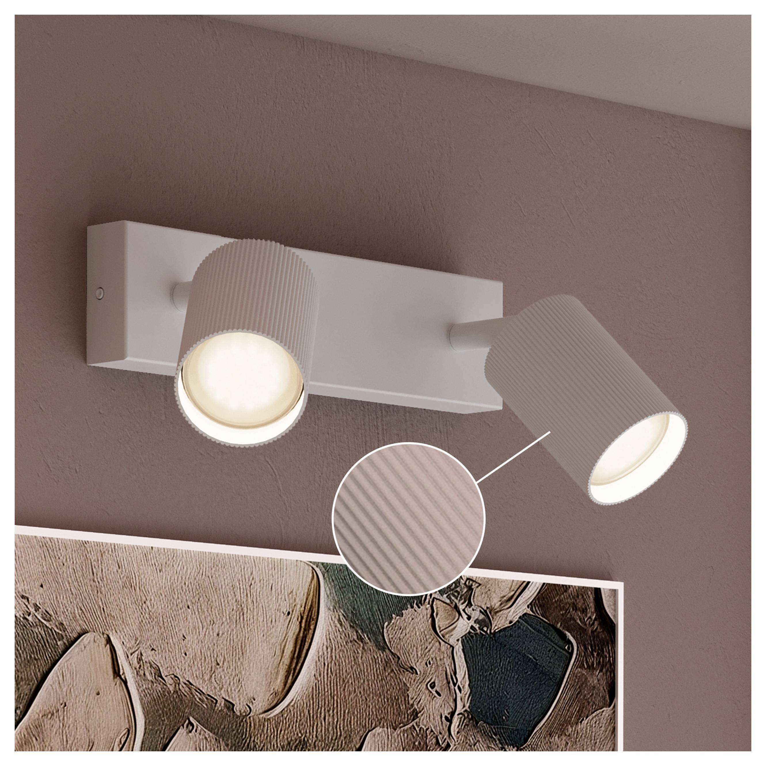 Zweiköpfige Wandleuchte in Weiß, mit beiden verstellbaren Lampen über Wandkunst an einer mauvefarbenen Wand leuchtet.