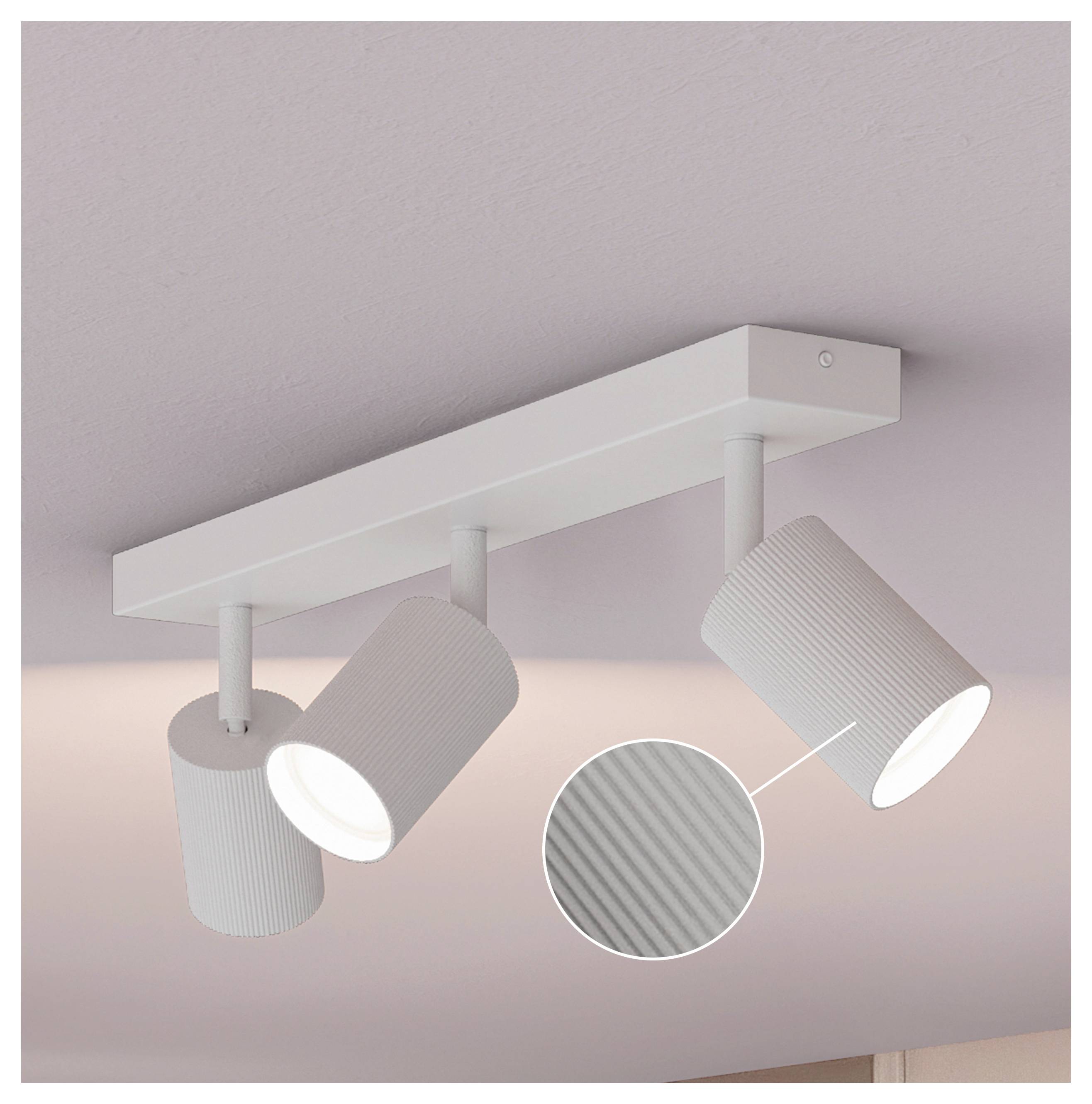 Weißes Drei-Leuchten-Deckenleuchten-System mit verstellbaren gerippten zylindrischen Spotlights auf einer hellrosa Decke; die Vergrößerung zeigt eine Nahaufnahme des strukturierten Schirms.