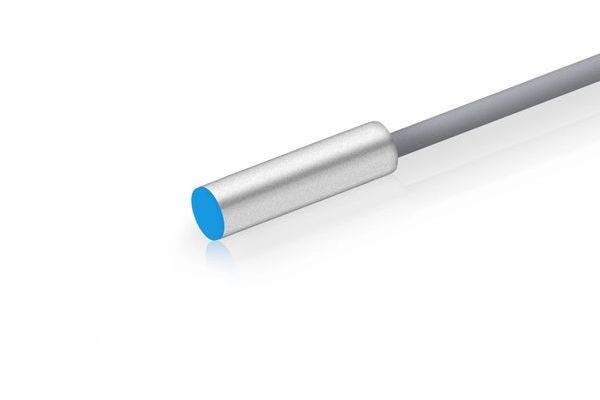 Nahaufnahme einer silbernen zylindrischen Sonde oder eines Sensors auf einem grauen Kabel, schräg gegen einen weißen Hintergrund gezeigt.