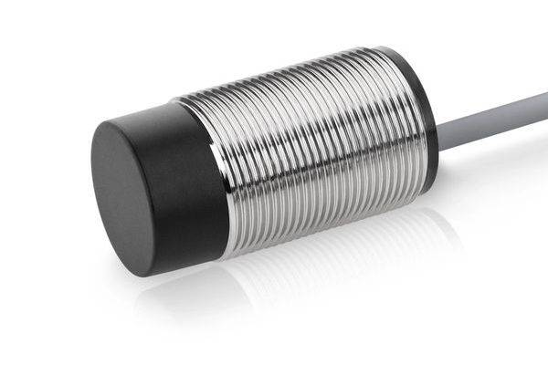 Nahaufnahme eines zylindrischen metallischen induktiven Näherungssensors mit einem Kabel, das sich von einem Ende erstreckt, isoliert auf weißem Hintergrund.