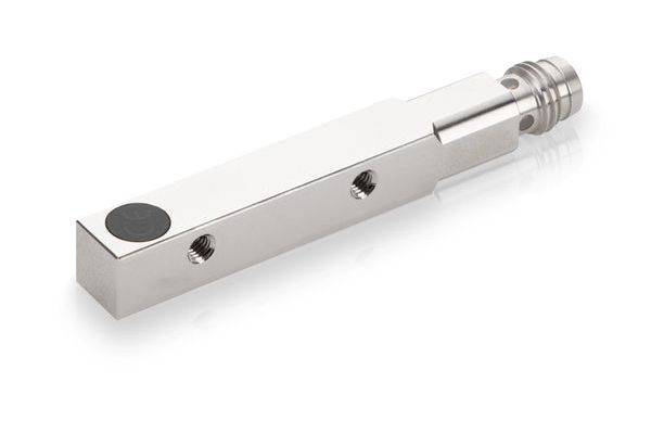 Metallische rechteckige Sensor- oder Aktorkomponente mit Gewindelöchern und einem zylindrischen Anschluss an einem Ende, dargestellt auf weißem Hintergrund.