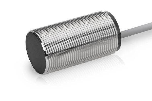 Nahaufnahme eines zylindrischen metallischen induktiven Näherungssensors mit einem Kabel, das sich von rechts erstreckt, isoliert auf weißem Hintergrund.