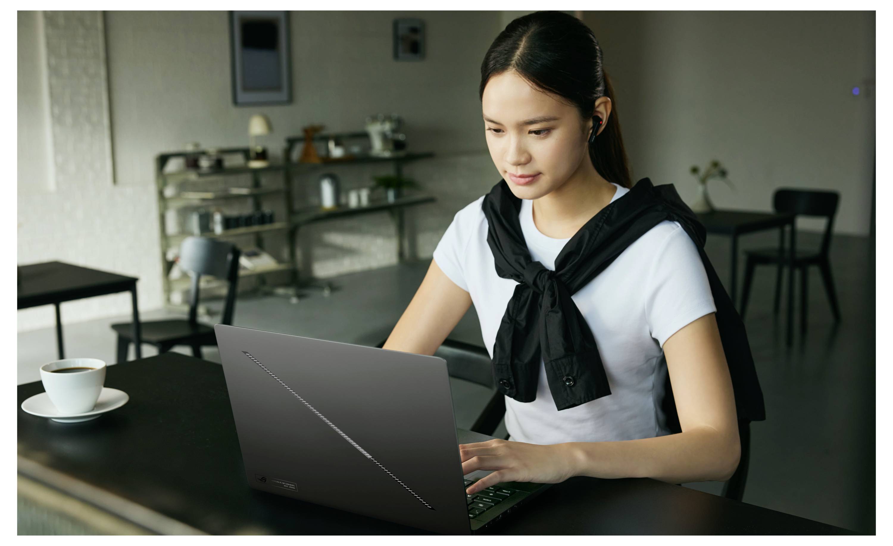 Junge Frau, die an einem Laptoptisch in einem Café arbeitet, mit einer Kaffeetasse neben ihr.