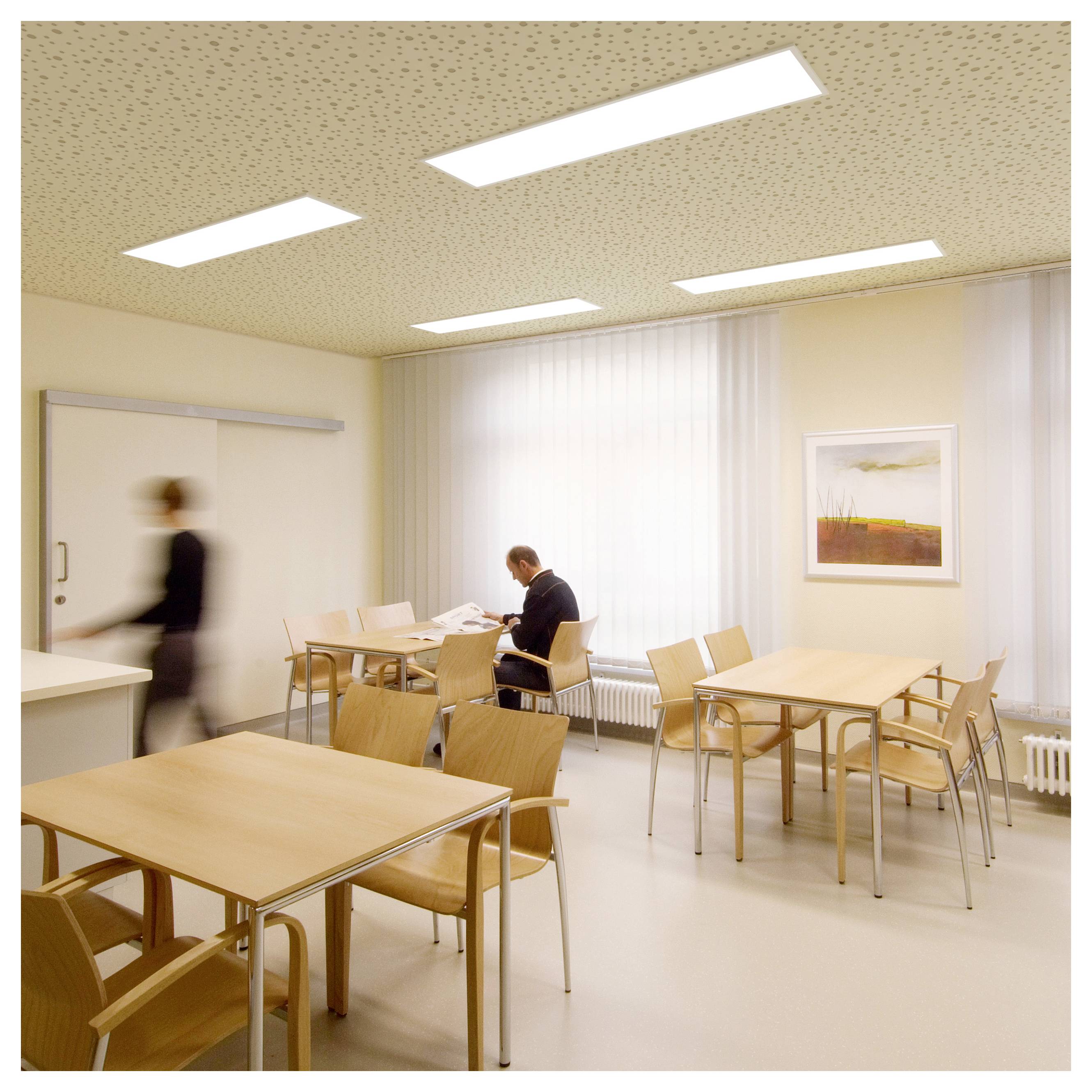 Helles Büro-Pausenzimmer mit Tischen und Stühlen; eine Person sitzt an einem Tisch und liest, während eine andere unscharfe Person an der Tür vorbeigeht.