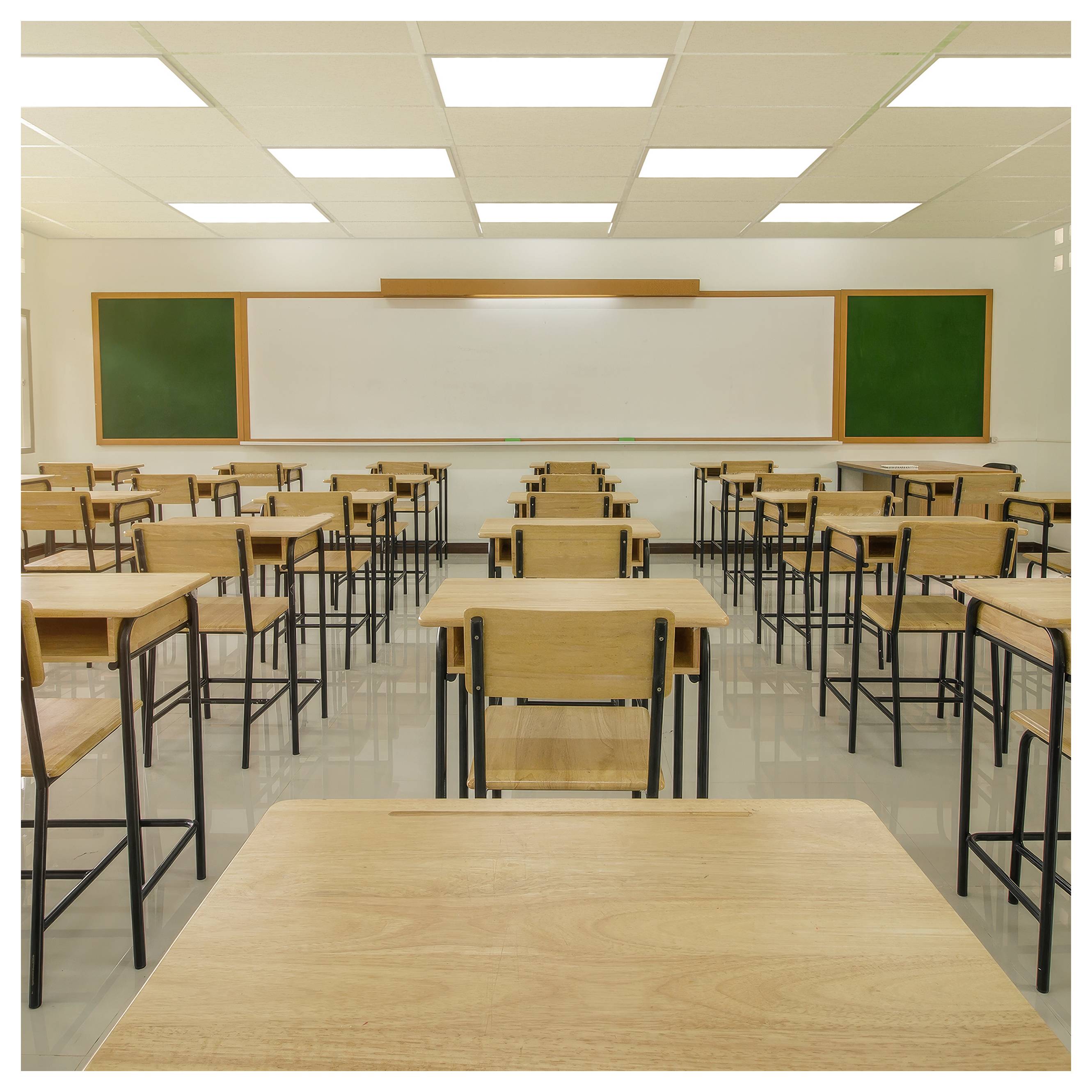 Leeres Klassenzimmer mit Reihen von Schreibtischen, die auf ein großes Whiteboard und zwei grüne Tafeln unter hellen Deckenleuchten ausgerichtet sind.