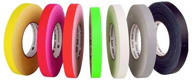 Sieben Rollen farbiges Klebeband nebeneinander angeordnet: gelb, beige, rosa, rot, grün, weiß, grau und schwarz.