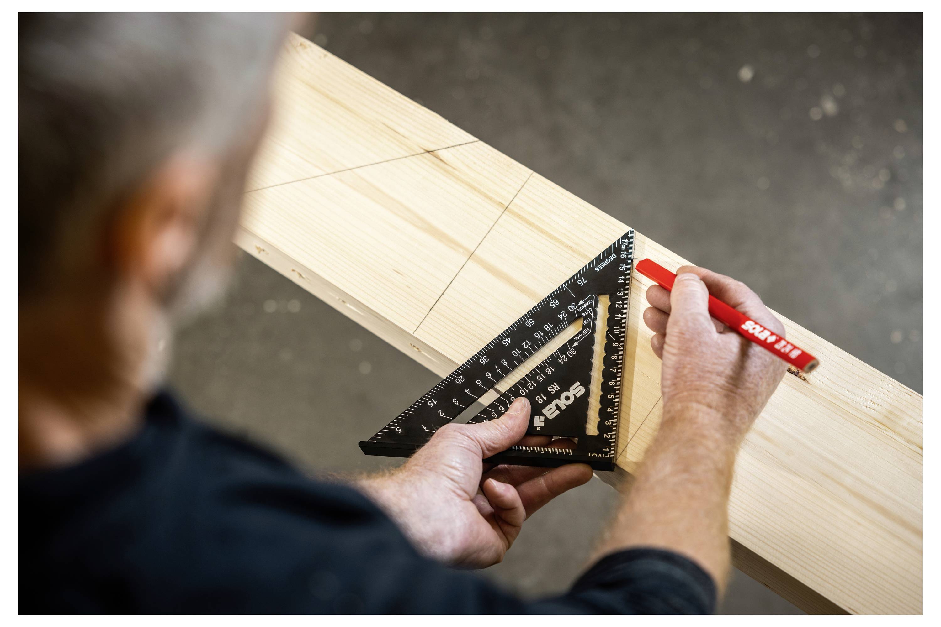 Eine Person markiert eine diagonale Schnittlinie auf einem Holzbrett mit einem Geschwindigkeitswinkel und einem roten Bleistift während der Schreinerarbeit.