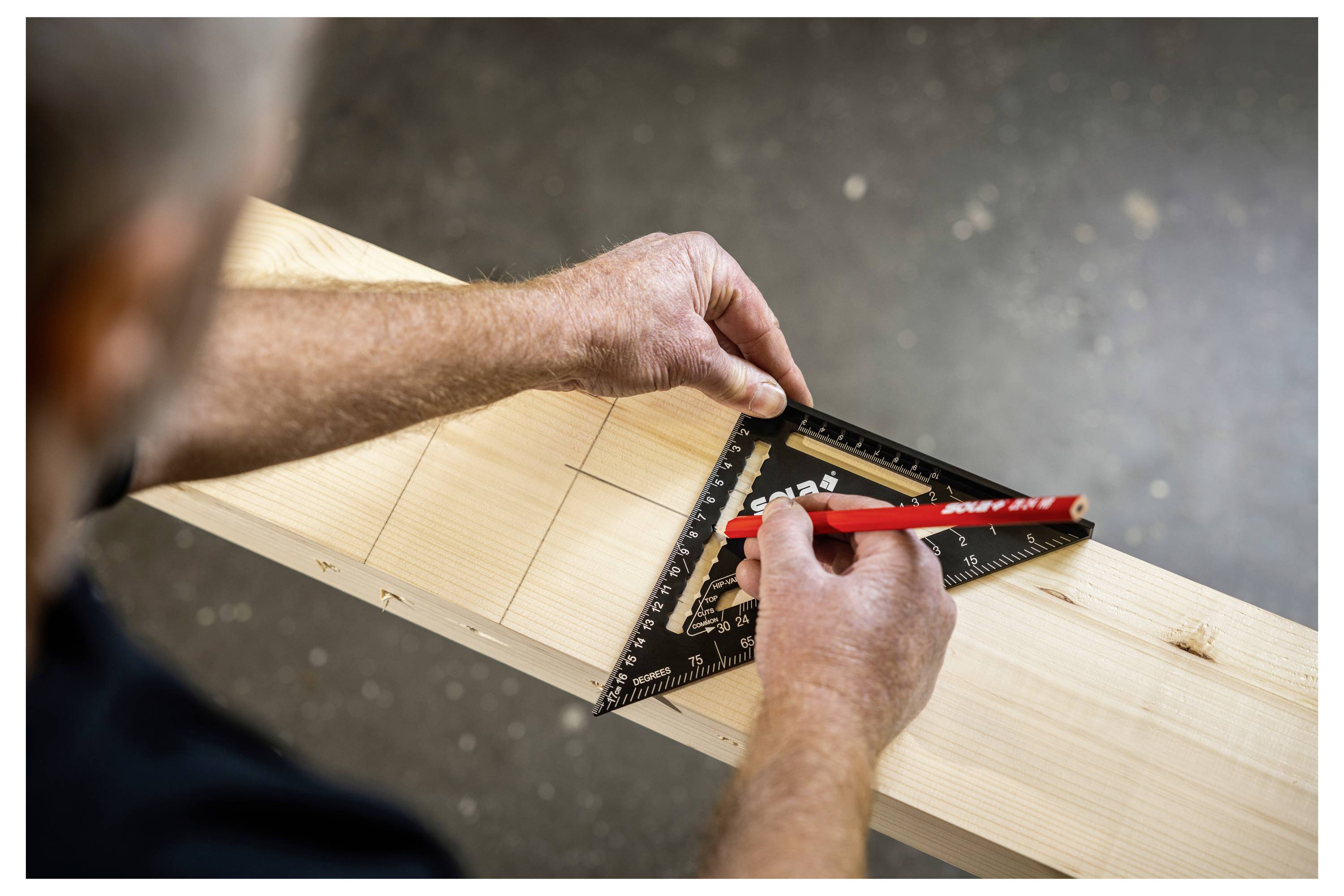 Hände markieren eine Schnittlinie auf einem Holzbalken mit einem Zimmermannswinkel und rotem Bleistift.