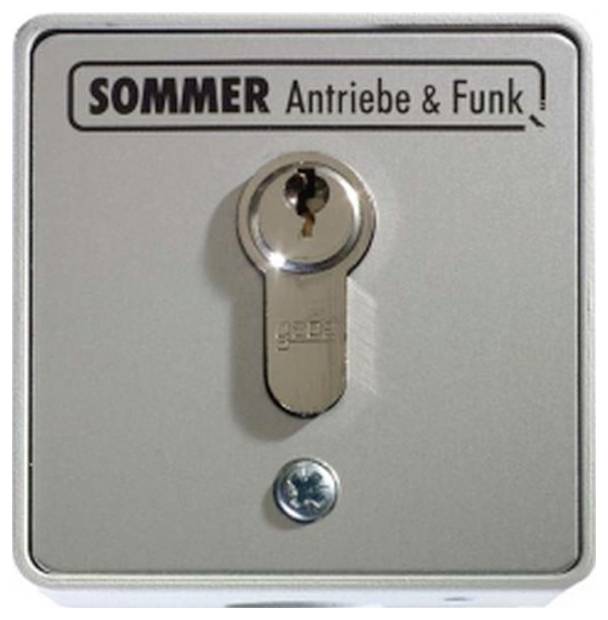 Metallverschloss- oder Schlüsselschalter-Panel mit der Beschriftung 'SOMMER Antriebe & Funk' mit einem eingefügten Schlüssel in der Mitte und einer Schraube darunter.