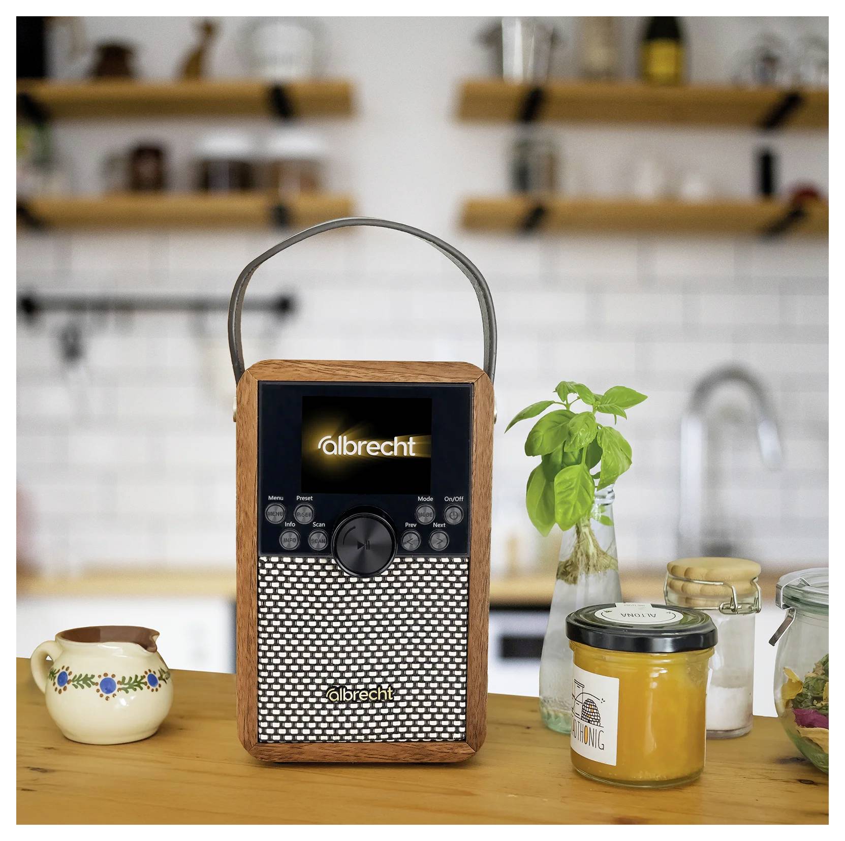Tragbares Albrecht-Radio mit Tragegriff auf einer Küchenarbeitsplatte, neben einer kleinen Pflanze, Gläsern und einer Tasse in einer unscharfen Küche.