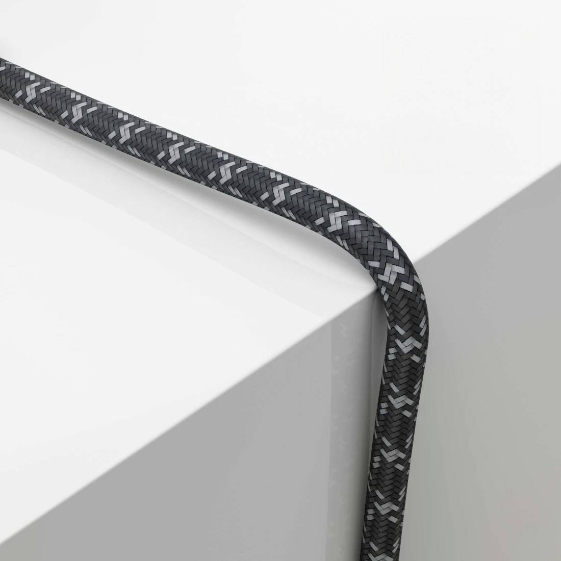 Schwarzes geflochtenes Kabel, das sich über die Ecke einer weißen Oberfläche biegt und an der Seite herunterh ängt.
