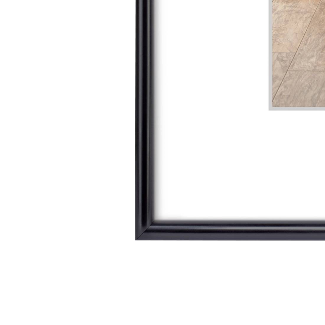 Nahaufnahme einer schwarzen Bilderrahmenecke auf weißem Hintergrund mit einem kleinen teilweisen beige-farbenen Kachelinset in der oberen rechten Ecke.
