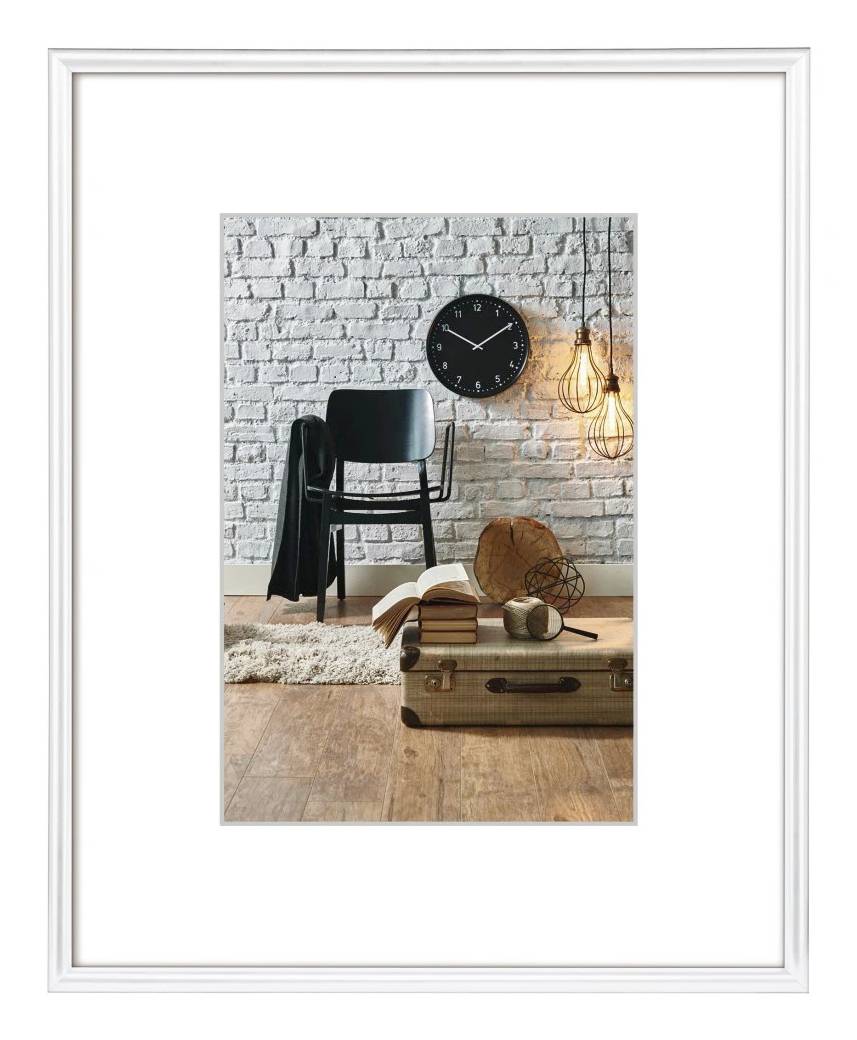 Stilvolle Raumvignette mit einem schwarzen Stuhl, einer Wanduhr, einer hängenden Glühbirne, Büchern und einem Vintage-Koffer auf einem Holzboden vor einer weißen Ziegelmauer.