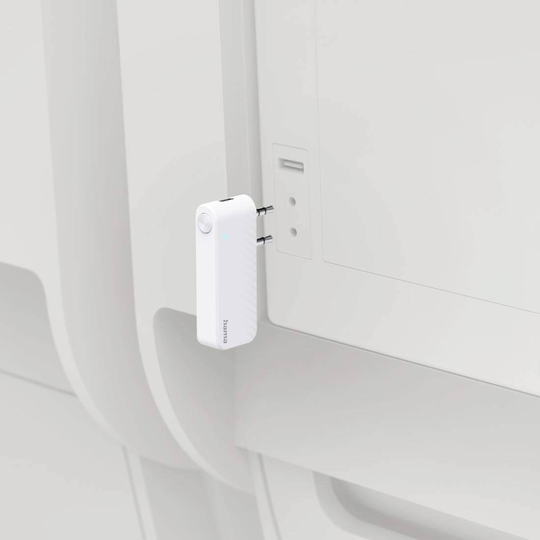 Weißer Stecker-Adapter oder Ladegerät, das in eine Wandsteckdose neben einem weißen Panel an einer sauberen, minimalistischen Innenwand eingesteckt ist.