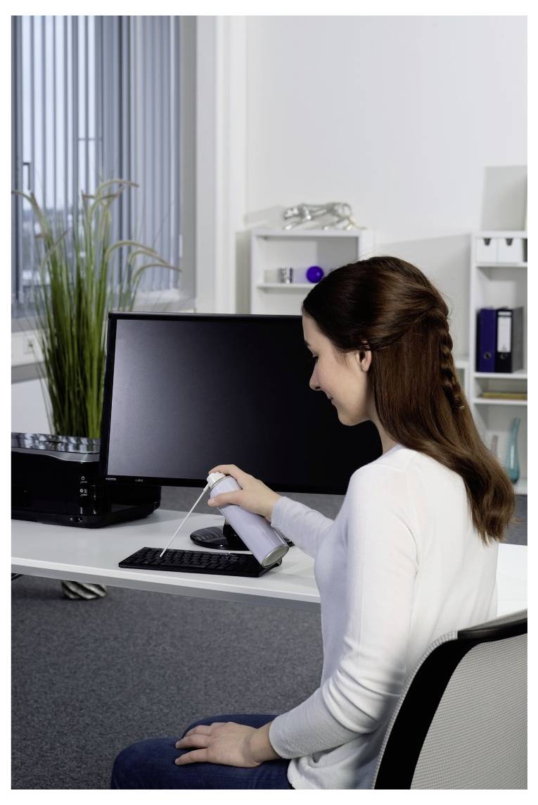 Eine Frau in einem Büro reinigt eine Computertastatur mit einem Tuch neben einem Monitor und Schreibtisch.