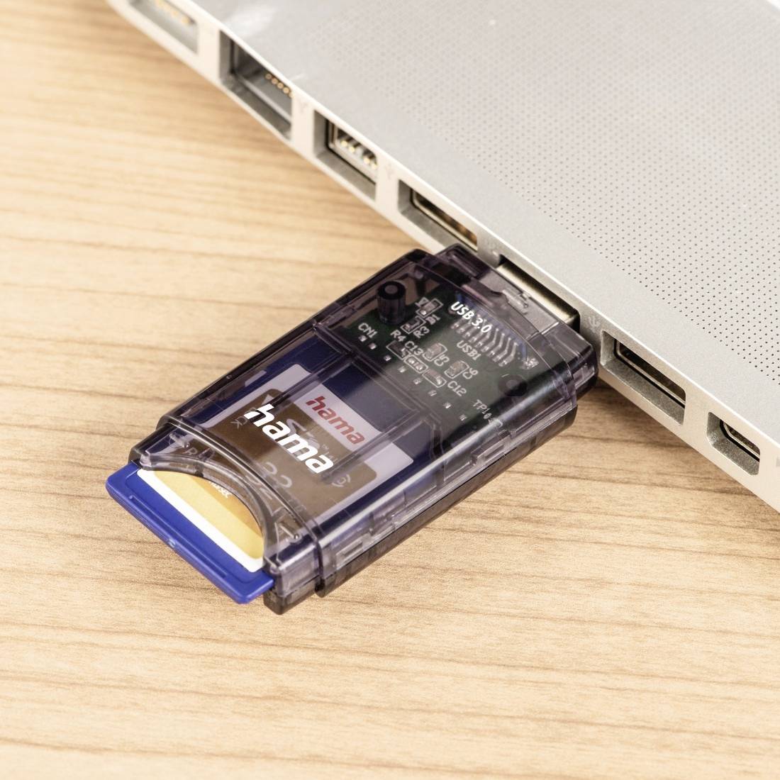 USB-Kartenleser in einen Laptop-Port auf einem Holztisch eingesteckt, mit einer eingelegten SD-Karte.