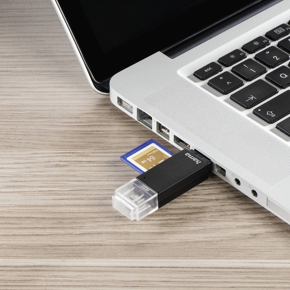 Ein USB-Stick und eine SD-Karte, die in die Seitenports eines Laptops auf einem Holzschreibtisch eingesteckt sind.