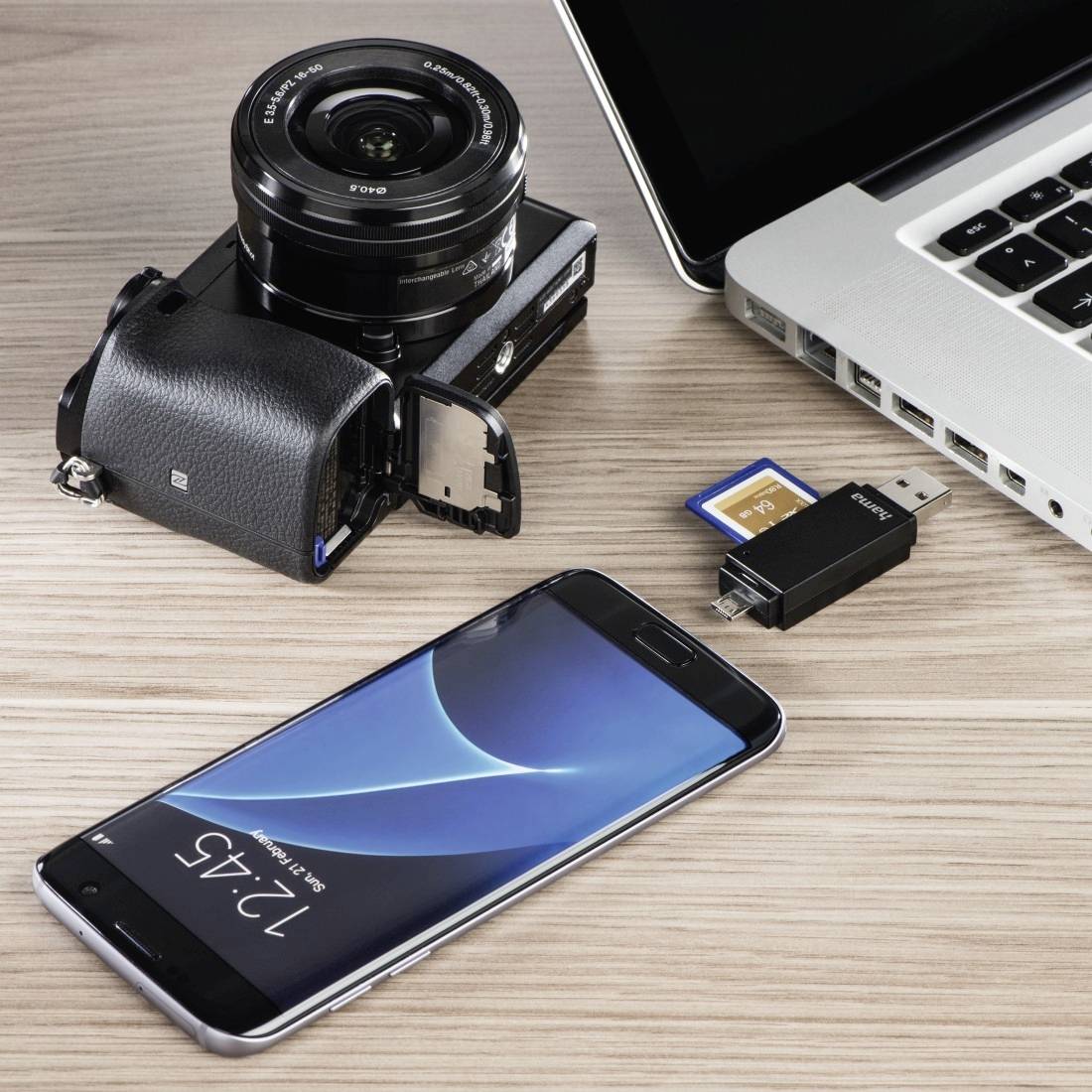 Eine Kamera mit Objektiv, Speicherkarten, USB-Stick, Smartphone und Laptop, die auf einem Schreibtisch angeordnet sind zum Übertragen oder Speichern von Fotos und Dateien.