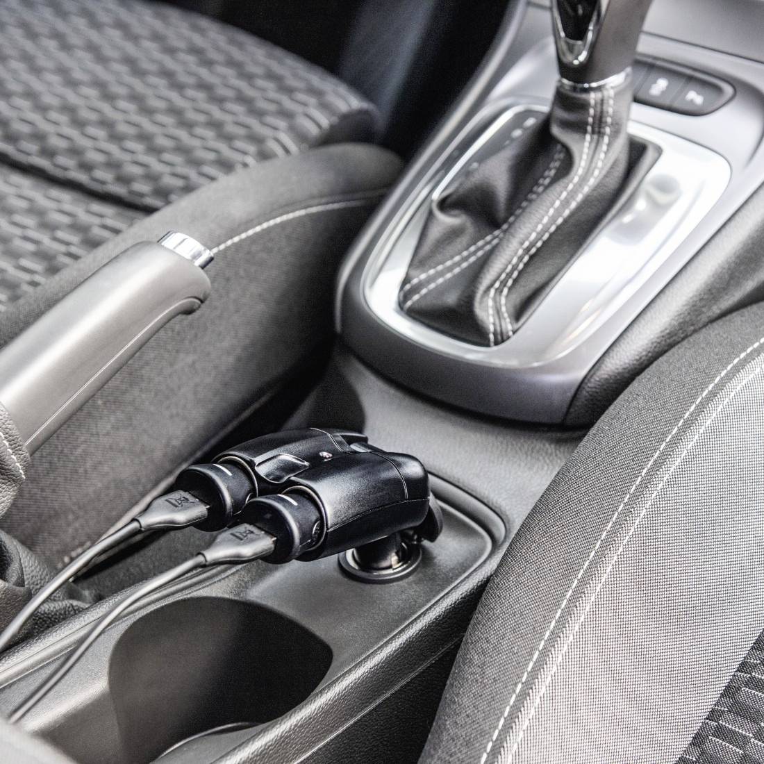 Mittenkonsole des Autos mit zwei eingesteckten Ladekabeln in einem Ablagefach neben der Schaltkulisse.