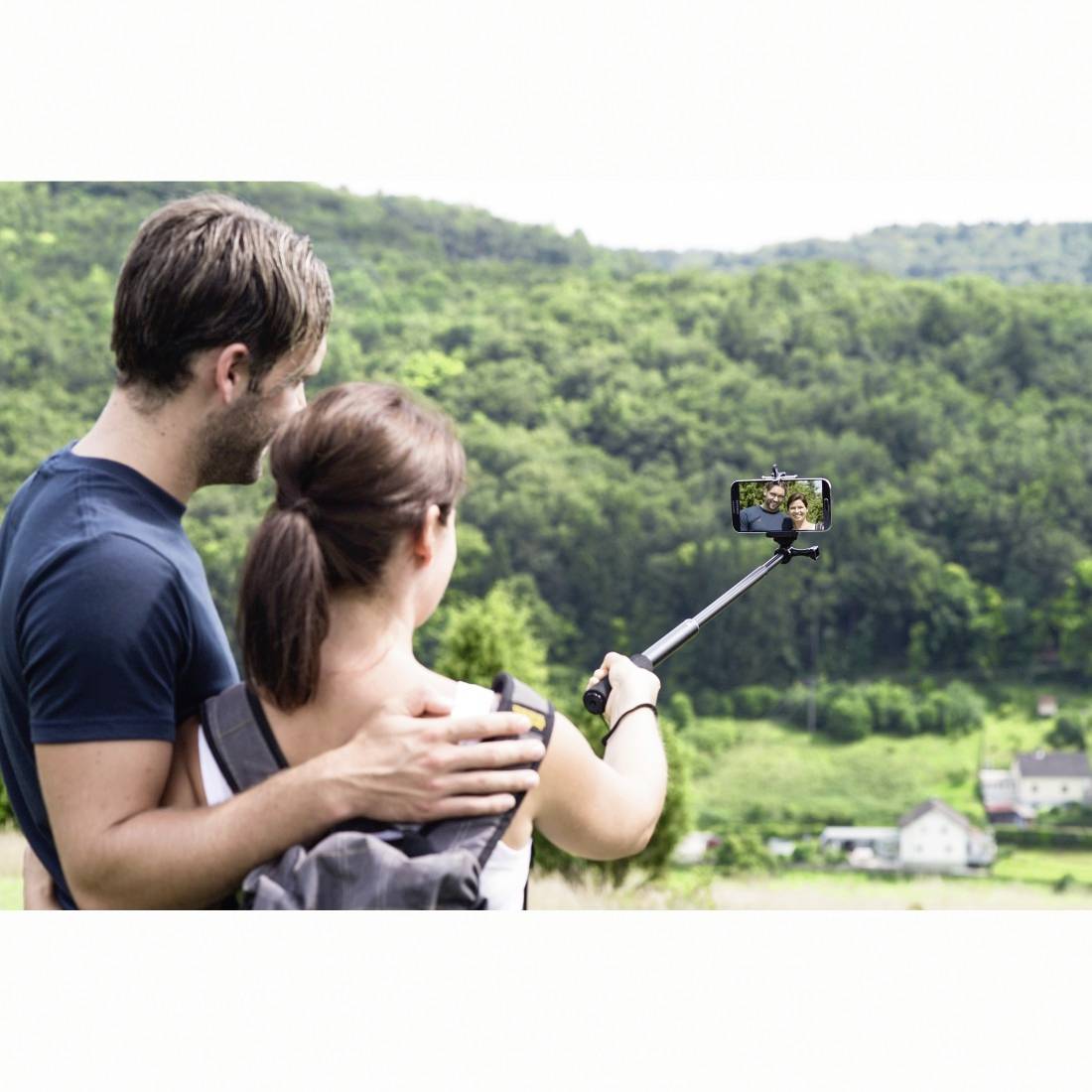Paar, das mit einem Selfie-Stick ein Selfie macht und dabei auf ein grünes Hügelland und Tal blickt