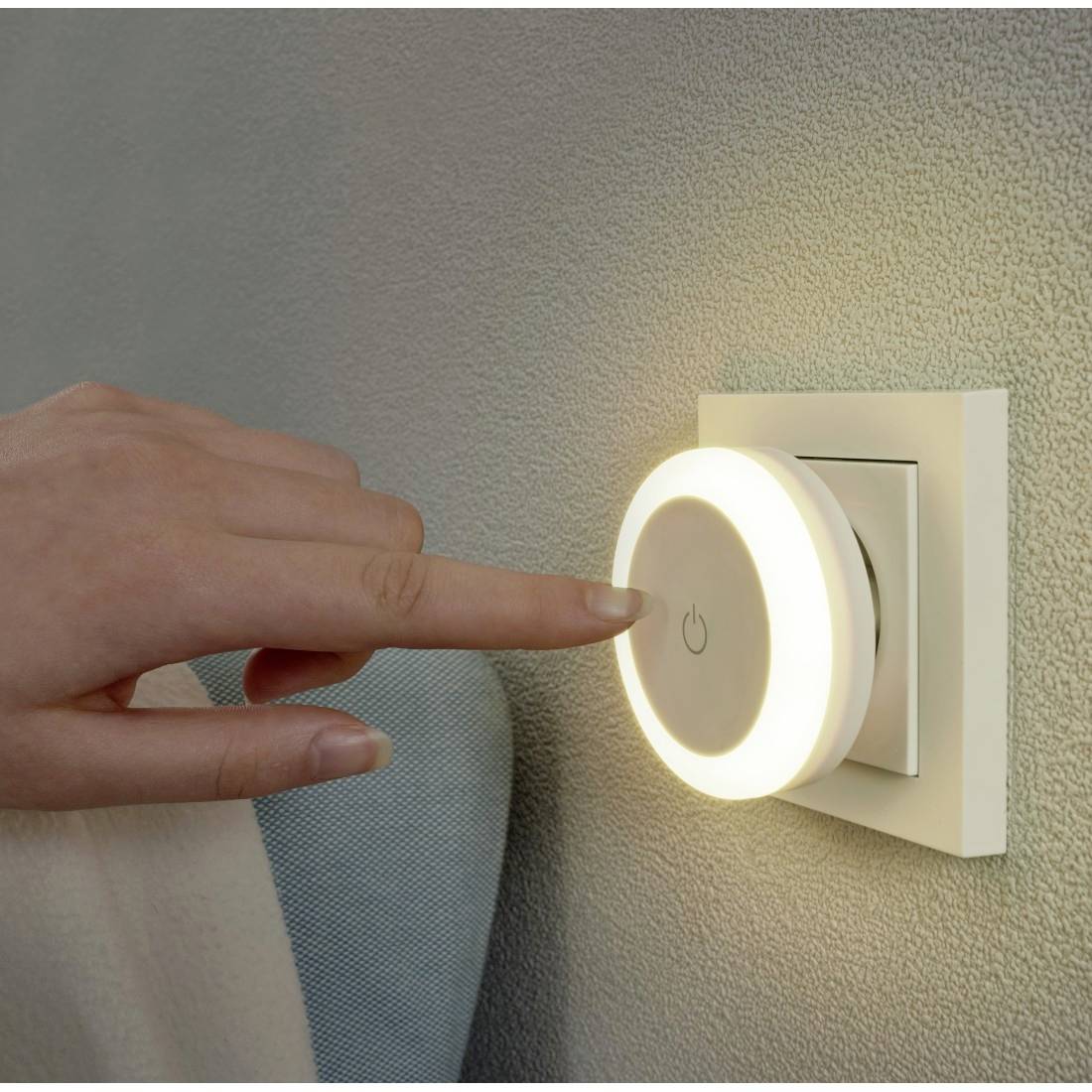 Hand drückt einen leuchtenden runden Wandlichtschalter auf einer strukturierten Wand.