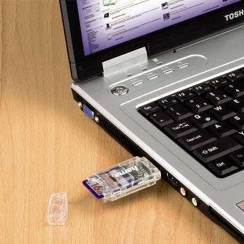 Ein Toshiba-Laptop auf einem Holzschreibtisch mit einem USB-Speicherstick, der in die Seite eingesteckt ist, und seiner Kappe, die in der Nähe liegt.