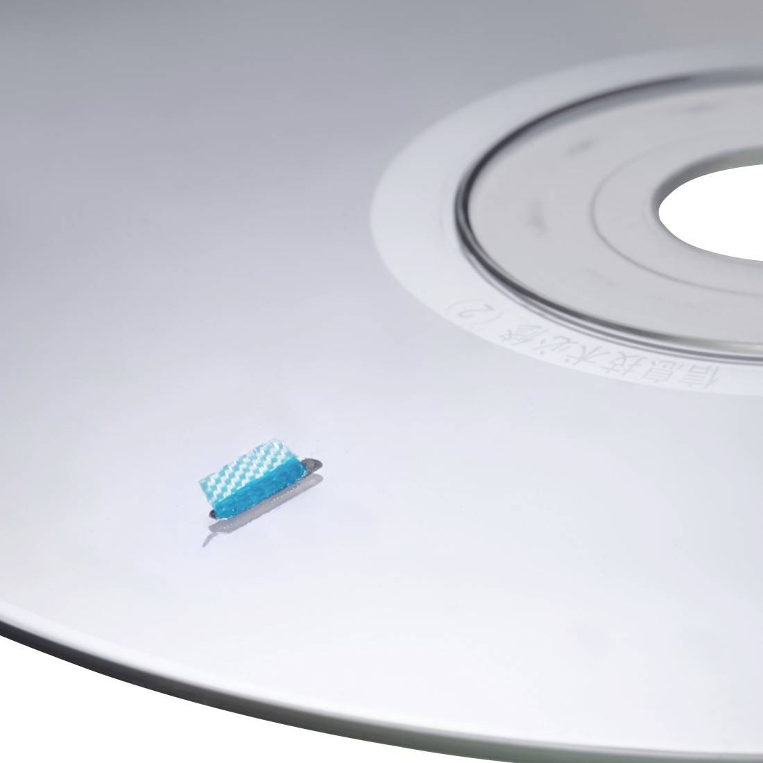 Ein blauer Reinigungsbürste ruht auf einer weißen CD oder DVD in der Nähe des Mittellochs.