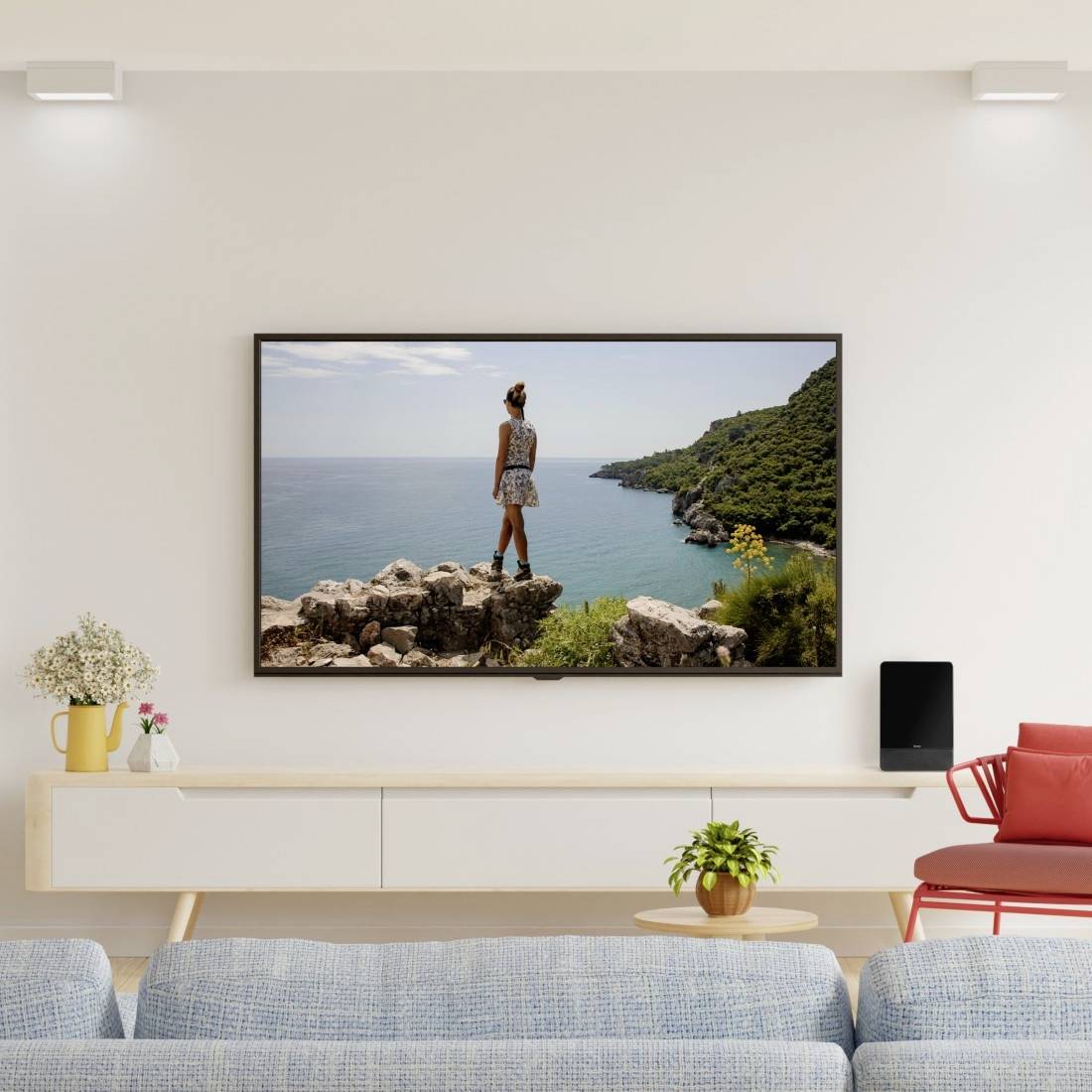 An der Wand montierter Fernseher zeigt eine Frau, die auf Felsen steht und auf das Meer und eine grüne Küstenlinie blickt, in einem modernen Wohnzimmer.