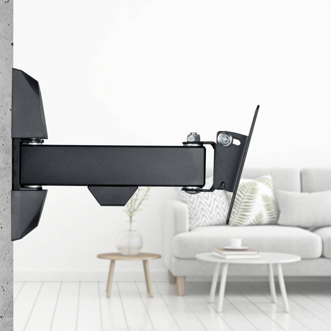 Wandmontierte Fernsehhalterung mit ausfahrbarem Arm in einem Wohnzimmer mit Sofa und Couchtischen im Hintergrund.