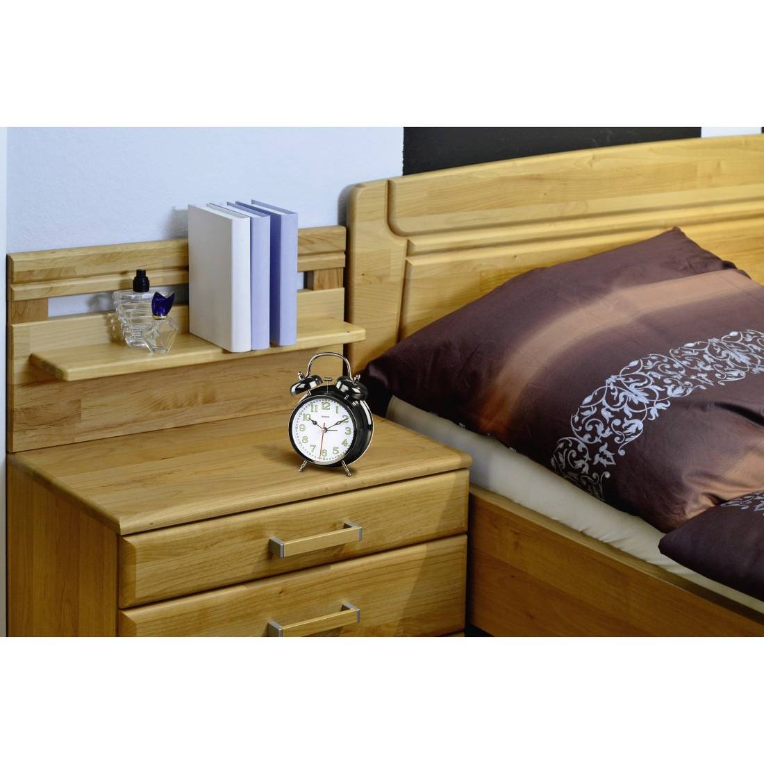 Schlafzimmernachttisch mit Wecker, Büchern und einem kleinen Glas; Holzbett mit brauner Bettwäsche daneben.