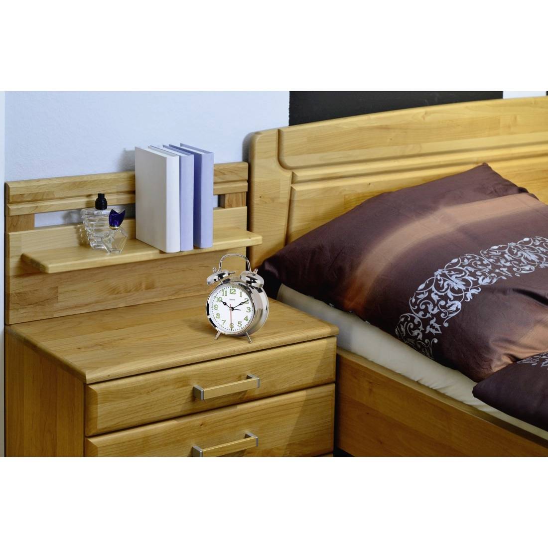 Holztisch neben dem Bett mit Wecker, Büchern und einem kleinen Glas neben einem Bett mit brauner Bettwäsche