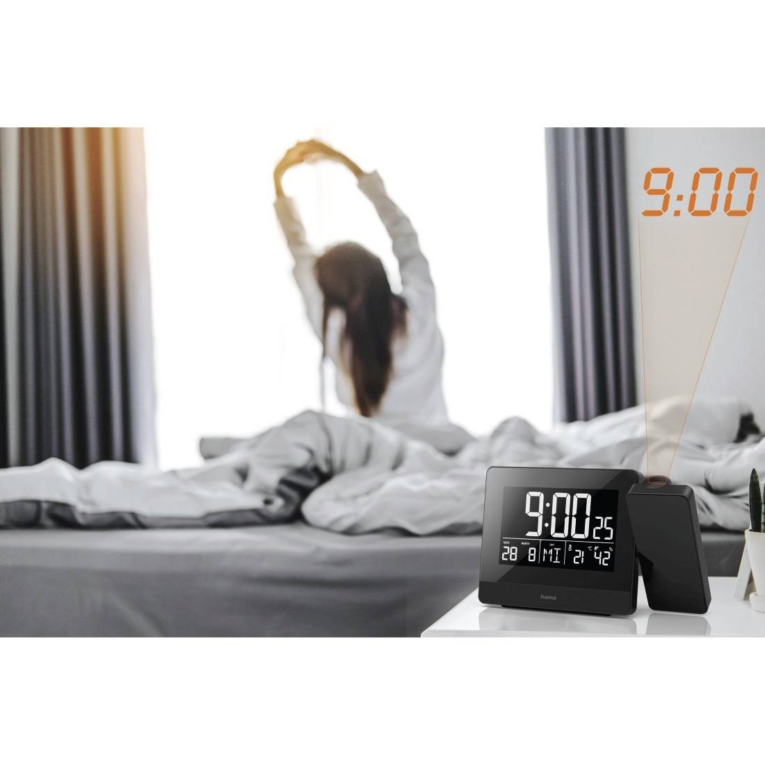 Digitale Wecker zeigt 9:00 Uhr auf einem Nachttisch an, mit einer Frau, die sich im Bett im Hintergrund streckt.