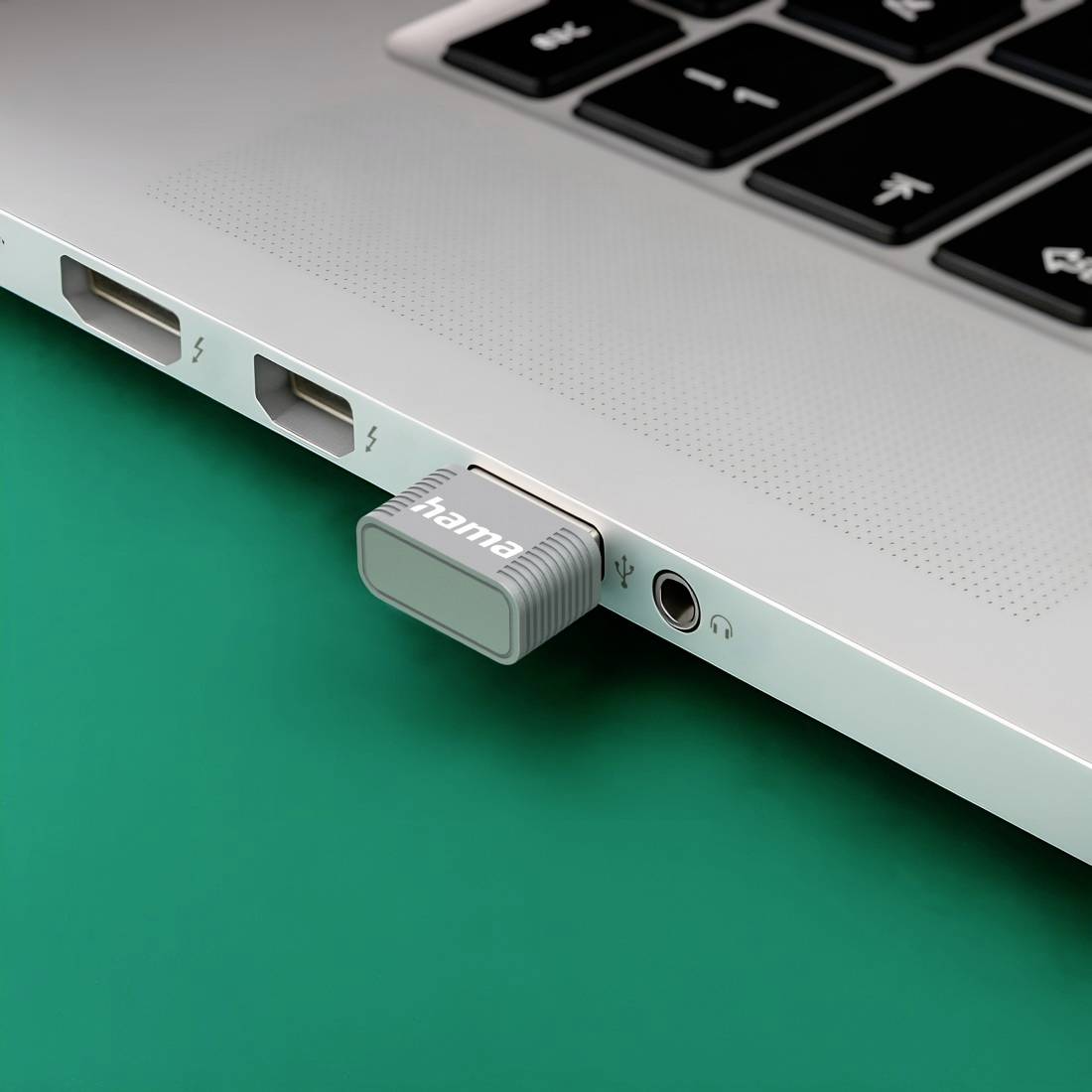 Nahaufnahme der Seite eines Laptops mit einem in den Anschluss gesteckten USB-C-Adapter, der sich auf einer grünen Oberfläche neben USB- und Kopfhöreranschlüssen befindet.