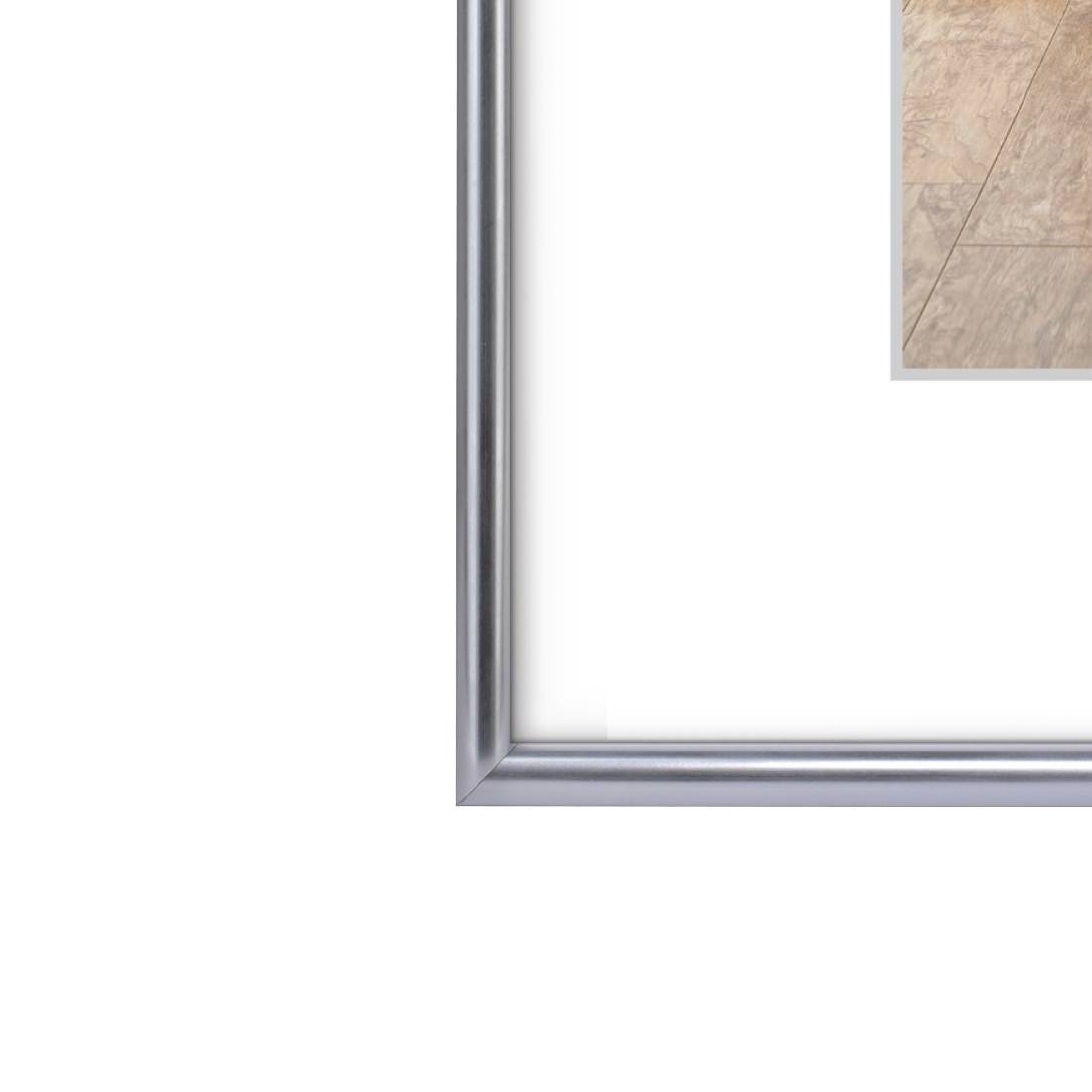 Nahaufnahme einer Ecke eines silbernen Bilderrahmens mit einem kleinen sichtbaren Kachelbild oben rechts auf weißem Hintergrund.