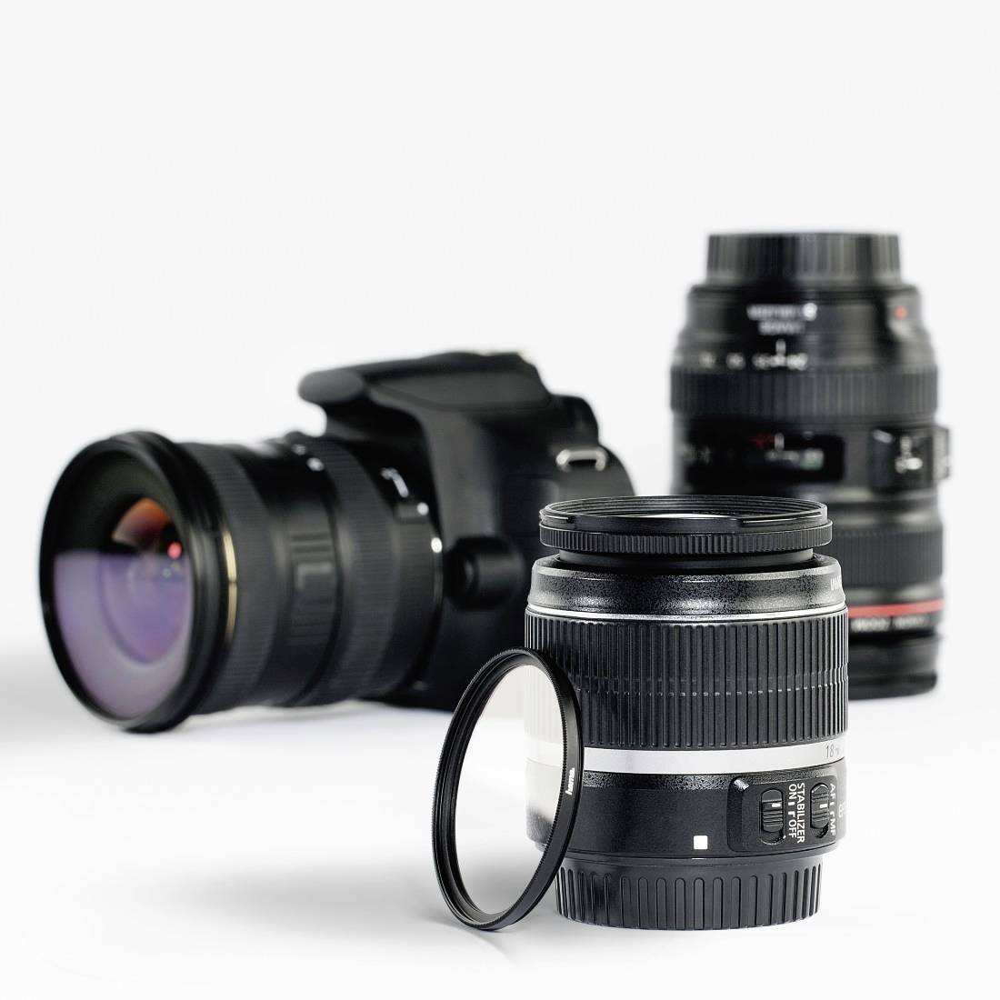 Kameraobjektive und eine DSLR-Kamera auf weißem Hintergrund, einschließlich eines Objektivfilters im Vordergrund.